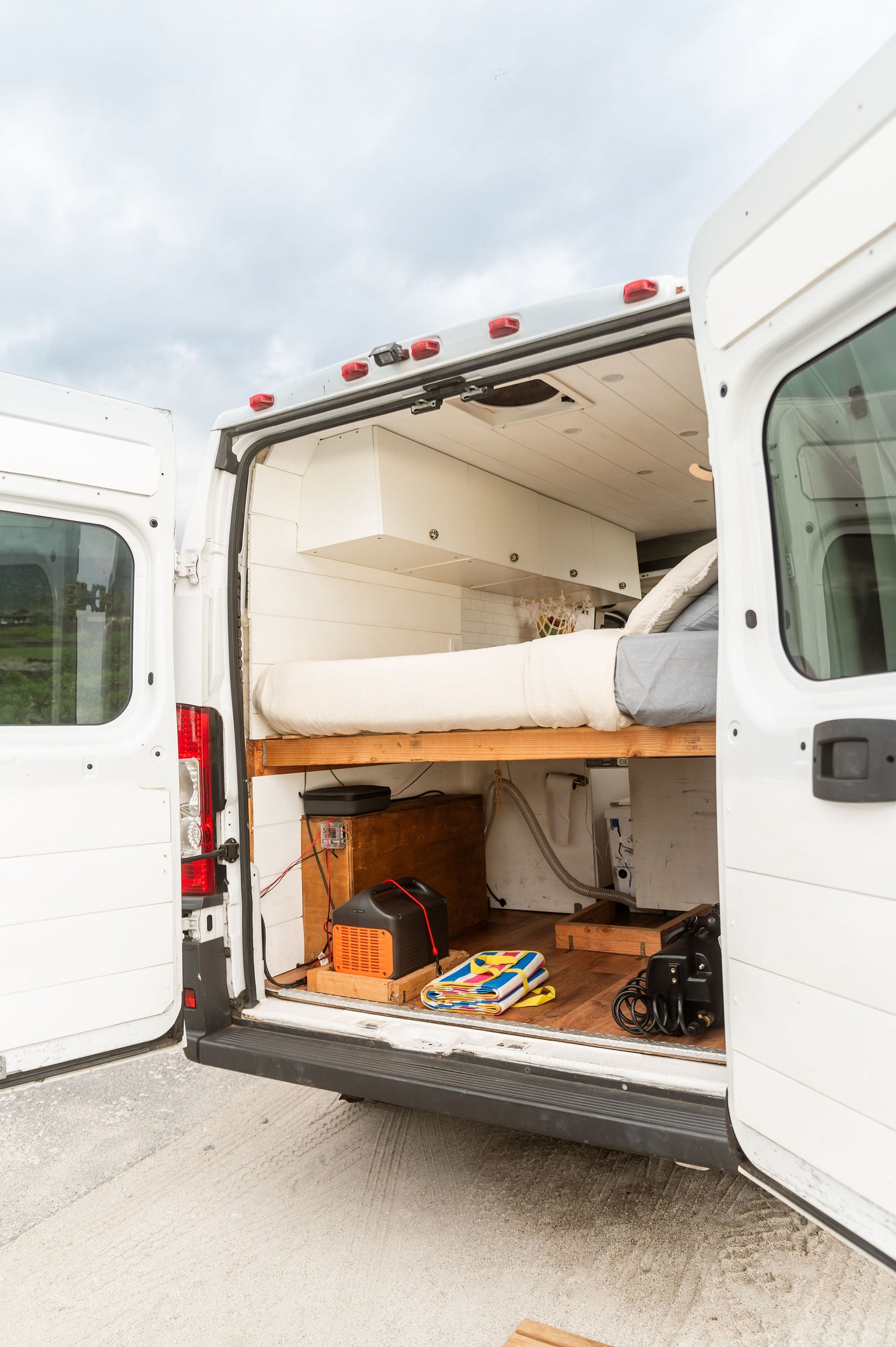 Open rear doors reveal an RV rental's clever van conversion: bed, storage, and off-grid setup, perfect for mobile living.