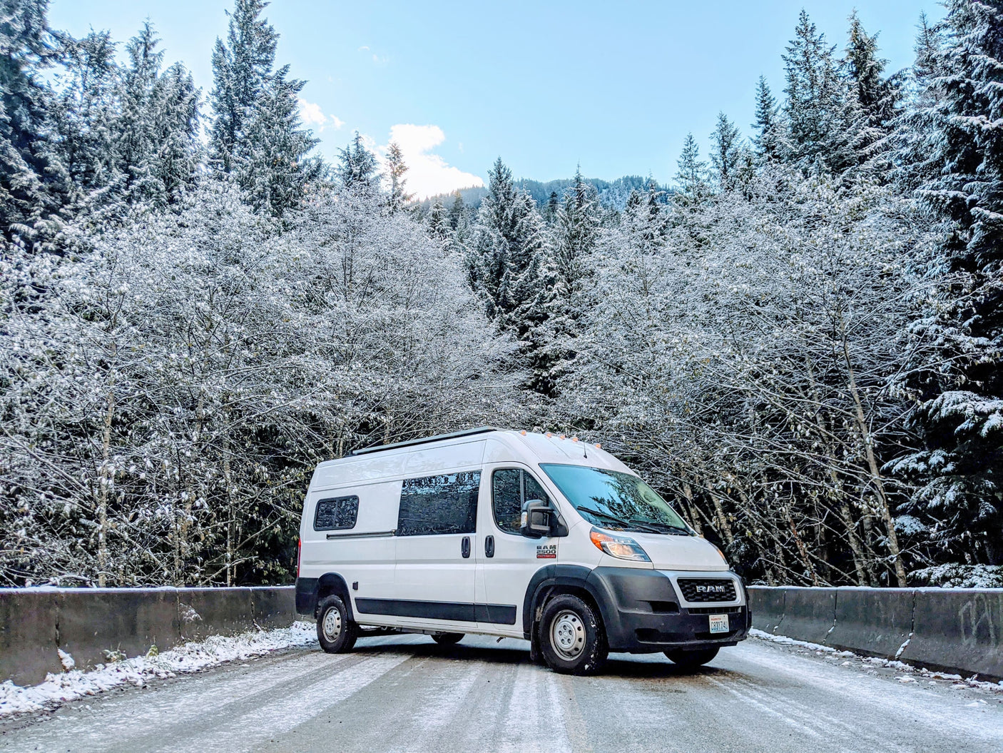 White RV rental van parked on a snowy road with beautiful snow-covered evergreen trees, ideal for winter adventures.