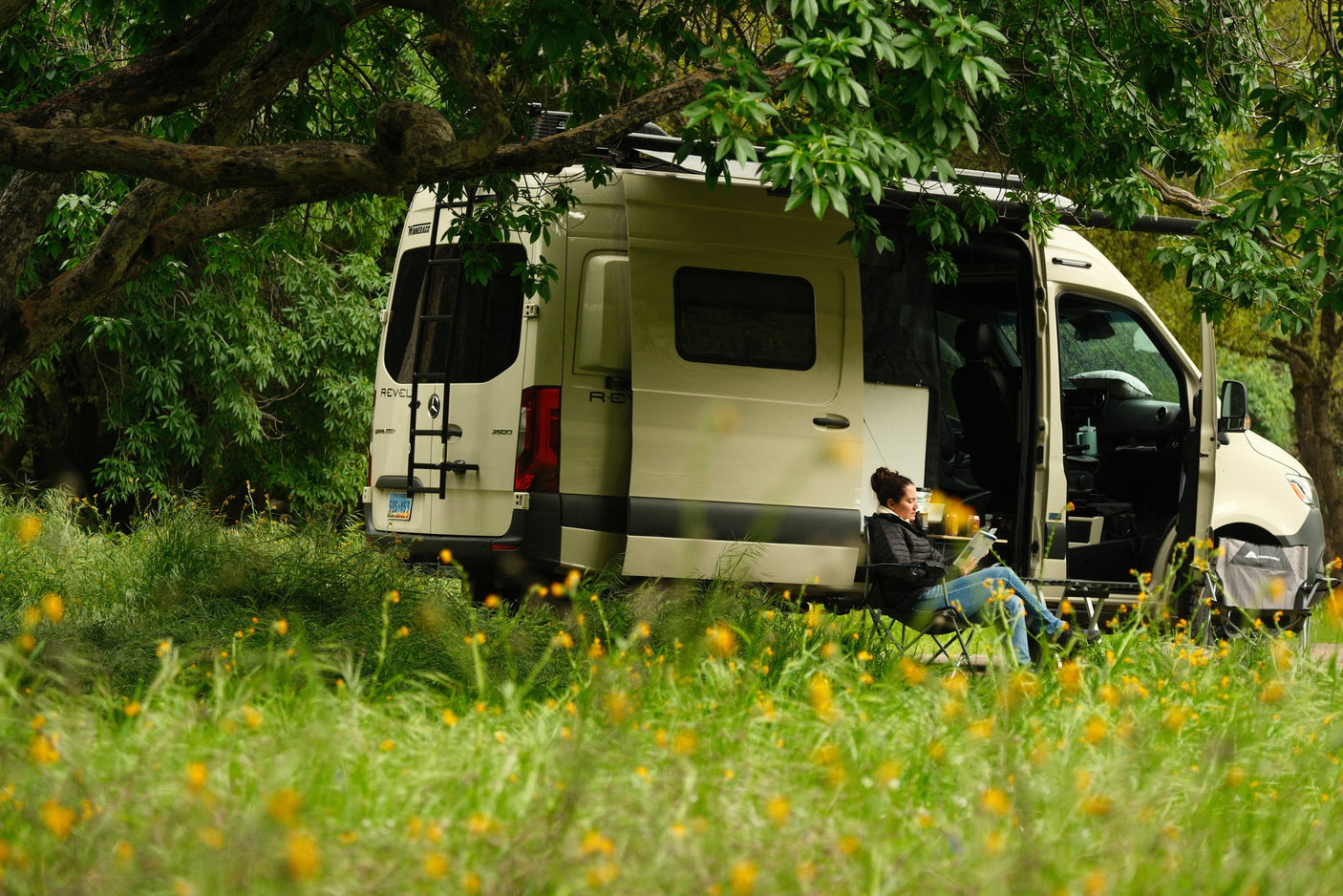 winding road through a lush green forest.|Relaxing rv rental: A woman reads by her Winnebago Revel camper van