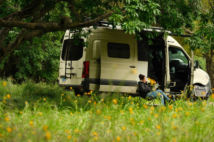 winding road through a lush green forest.|Relaxing rv rental: A woman reads by her Winnebago Revel camper van