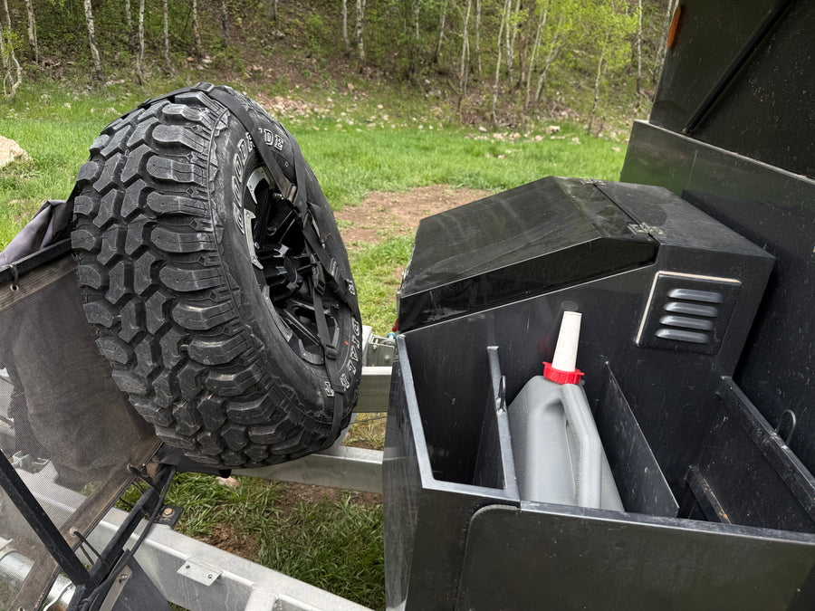 RV rental's rugged spare tire & storage box with jerrycan, set against a wooded backdrop.