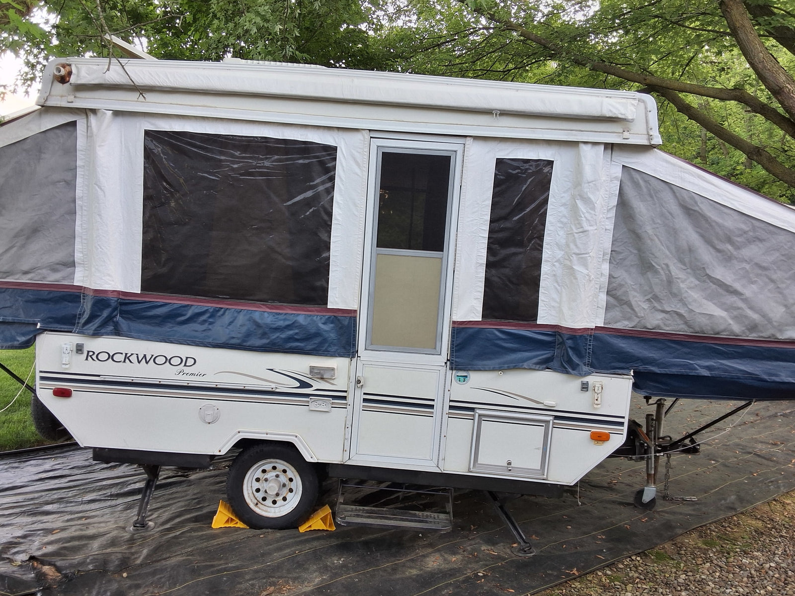 A white Rockwood Premier pop-up RV rental is set up on a black tarp, ready for outdoor camping adventures.