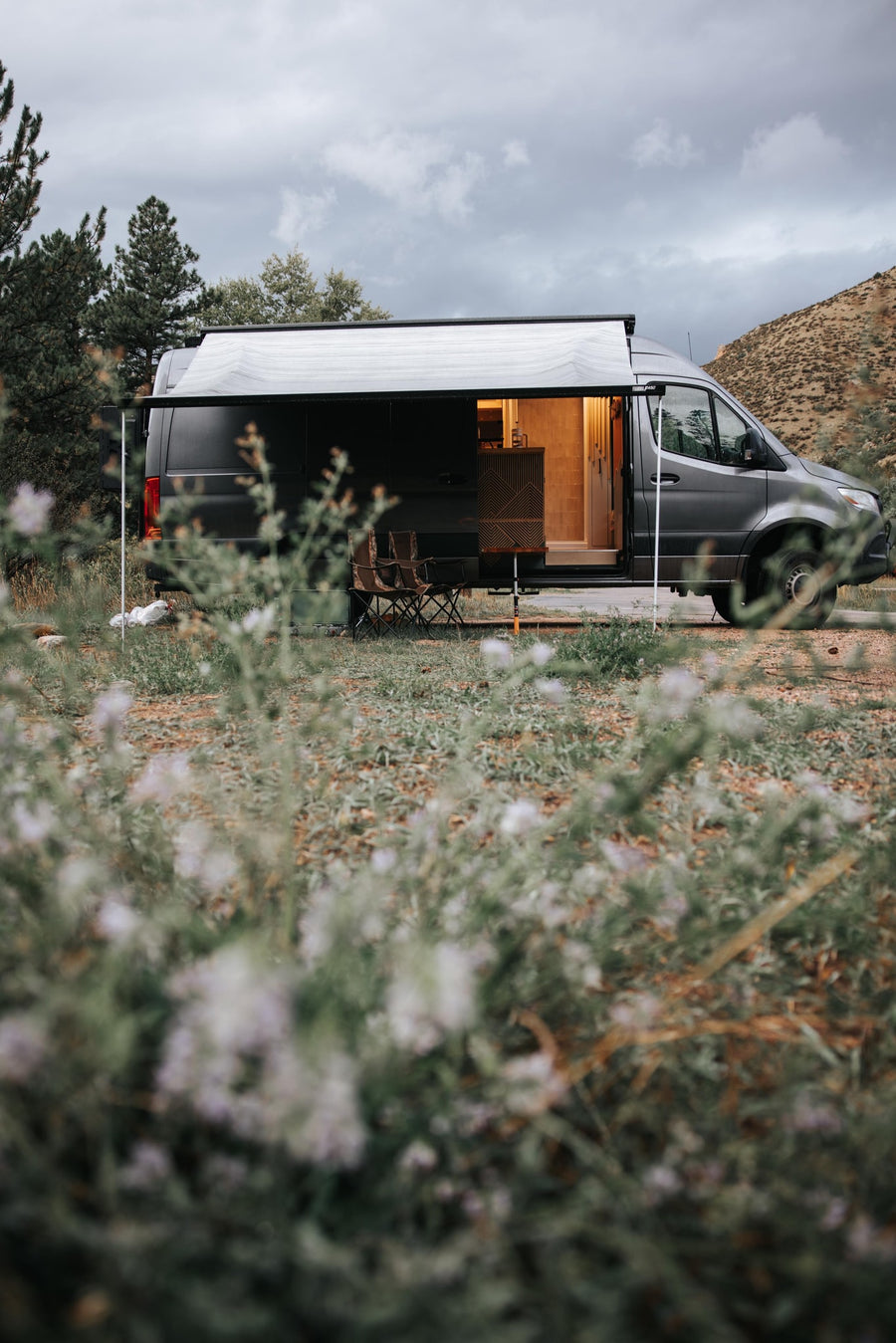 lit interior. Camping chairs invite outdoor relaxation in nature.|RV rental: This custom Sprinter camper van is parked on a sandy beach by the ocean