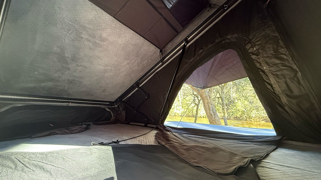 This RV rental's rooftop tent offers a sleeping area, integrated lighting, and a beautiful window view of trees & water.