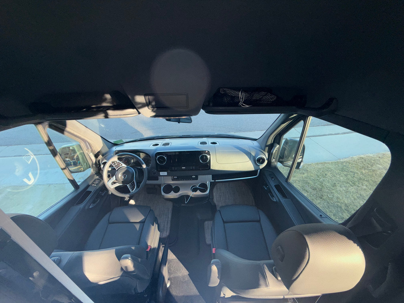 Interior of an RV rental: Wide view of the spacious front cabin with dashboard, steering wheel, and two front seats.