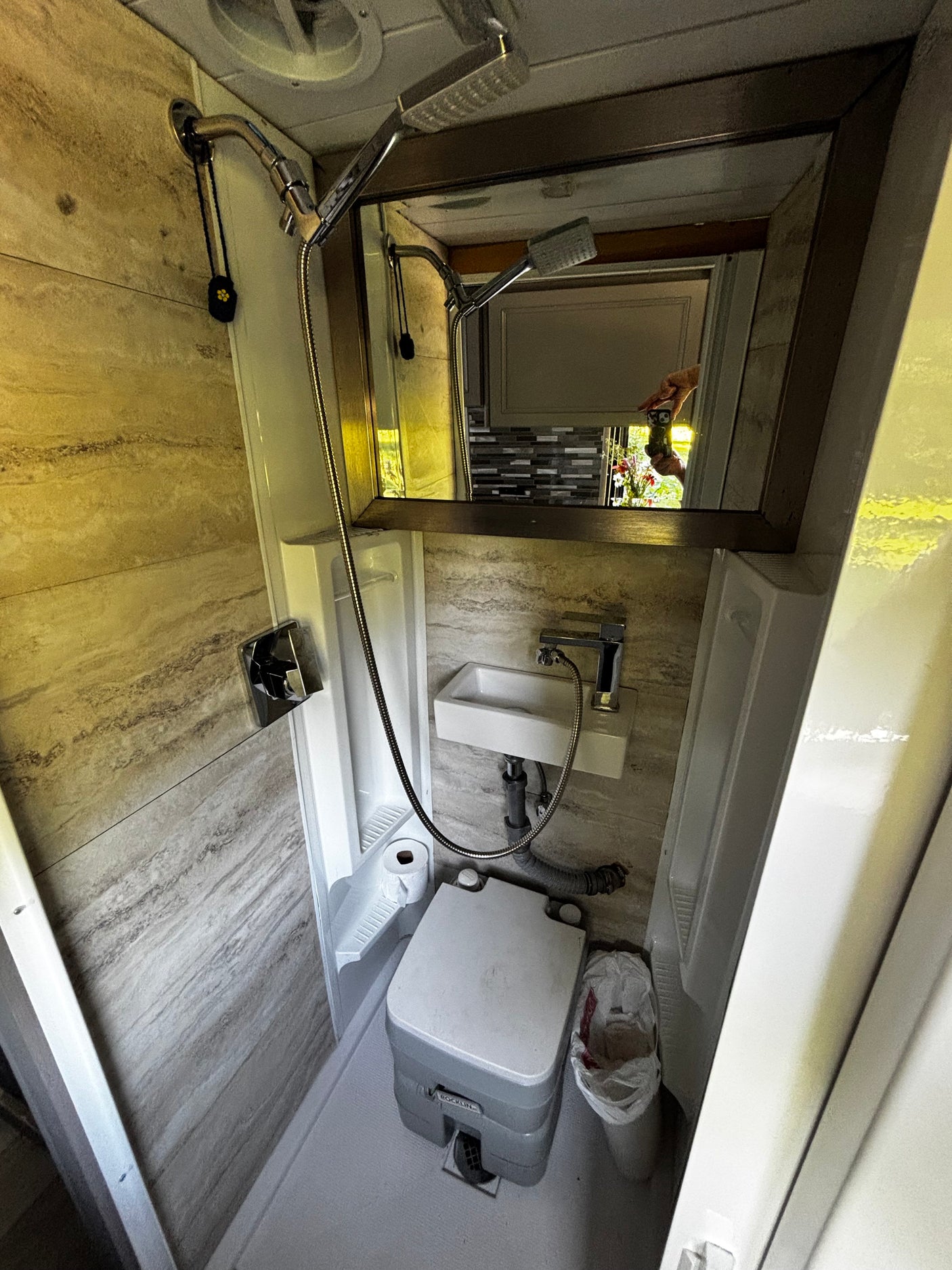 This compact RV rental bathroom features a shower, sink, portable toilet, and tiled walls.