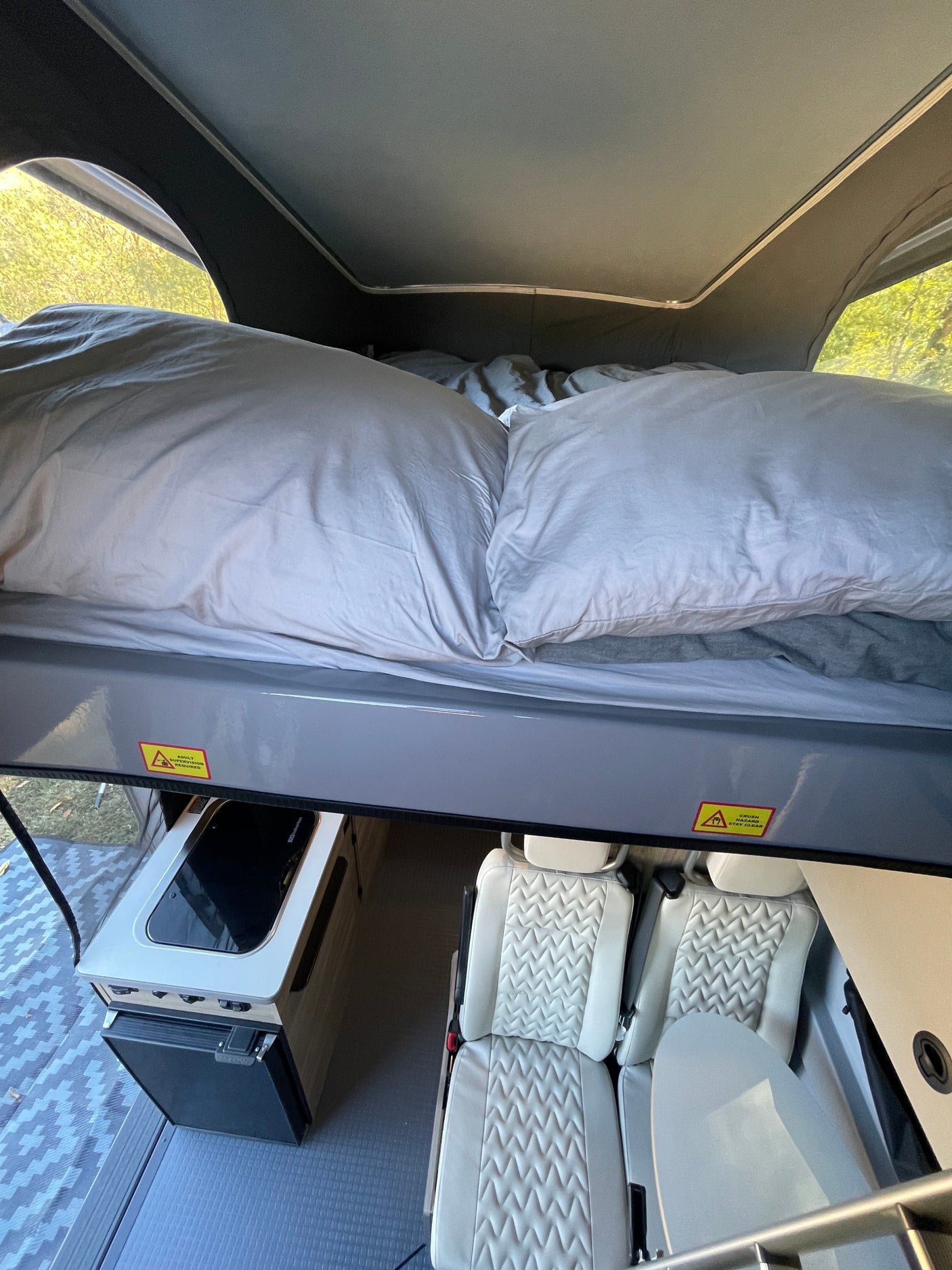 This RV rental features a multi-level design with a pop-top bed above a kitchen unit and quilted seats.