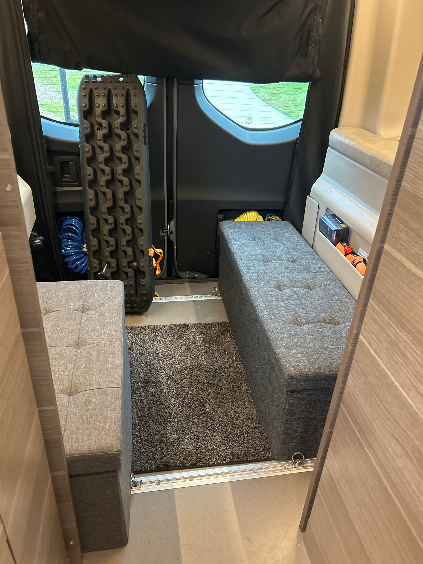 RV rental interior: two grey storage benches, rug, and essential off-road recovery gear like traction boards.