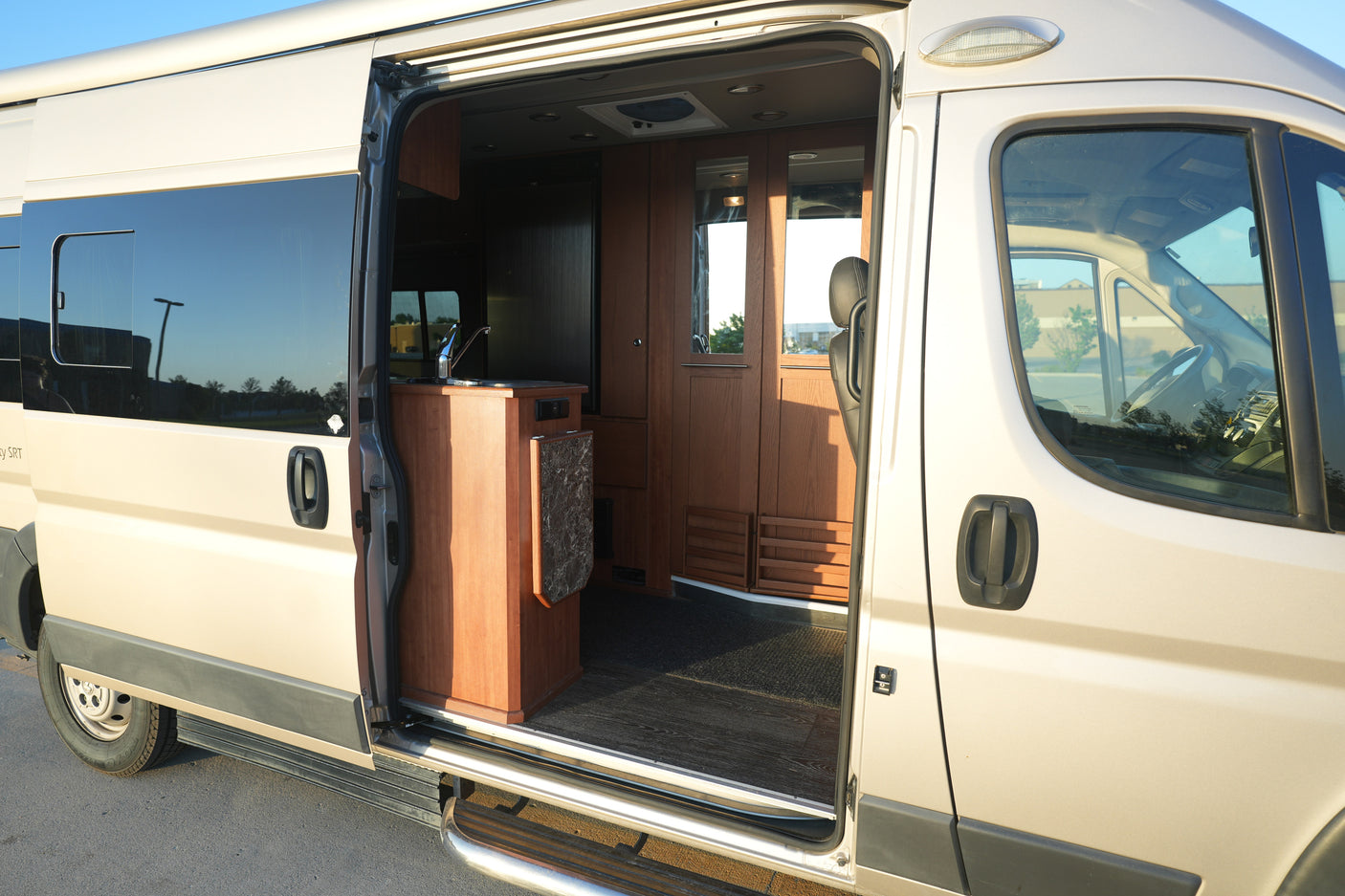 Tan rv rental camper van with open side door, revealing an interior kitchenette with a sink and wooden cabinets.