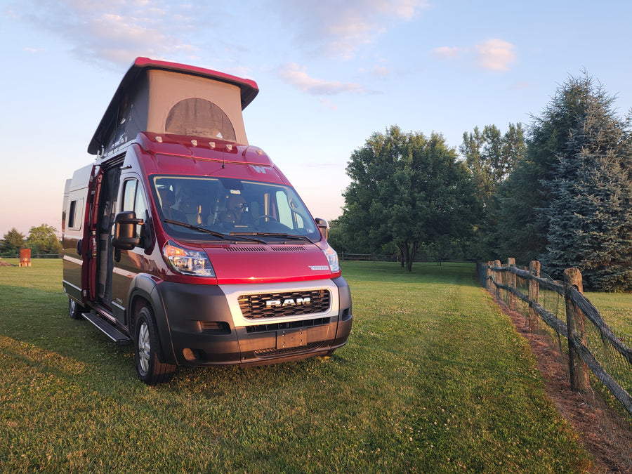 Red Winnebago camper van RV rental, pop-top open, ready for adventure on a grassy field at golden hour.
