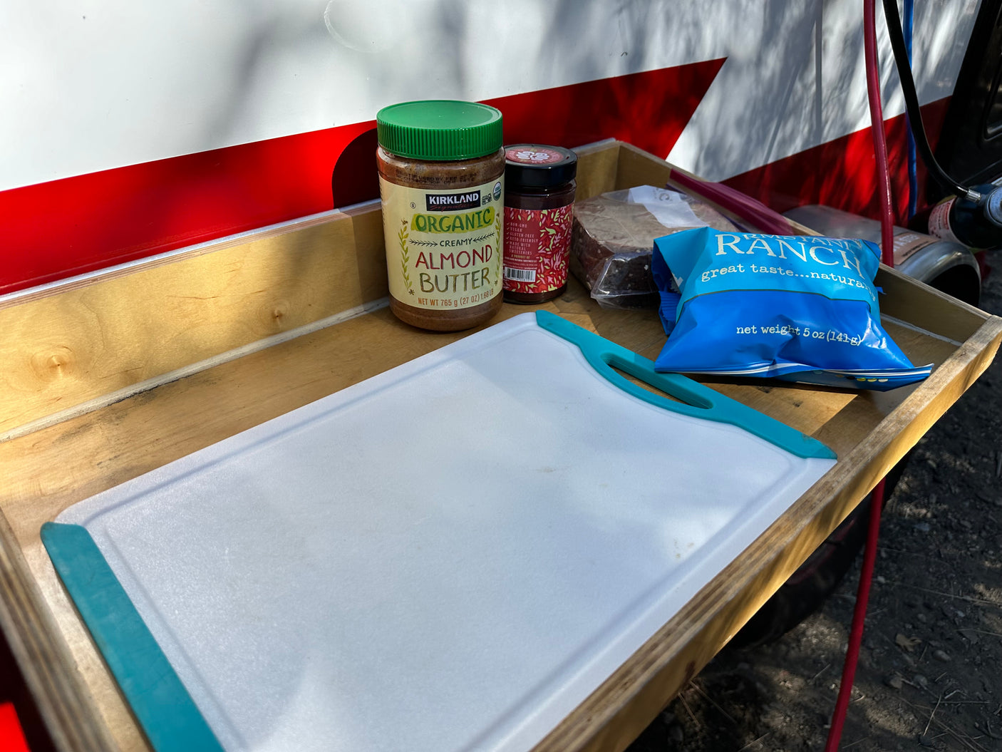 Preparing snacks on an RV rental pull-out tray: almond butter, jam, chips, and a cutting board for easy camping meals.