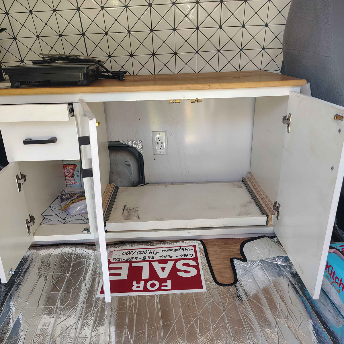 RV rental interior: a neat camper kitchen with white cabinets, pull-out storage, an electrical outlet, and stylish geometric tile. — photo 10