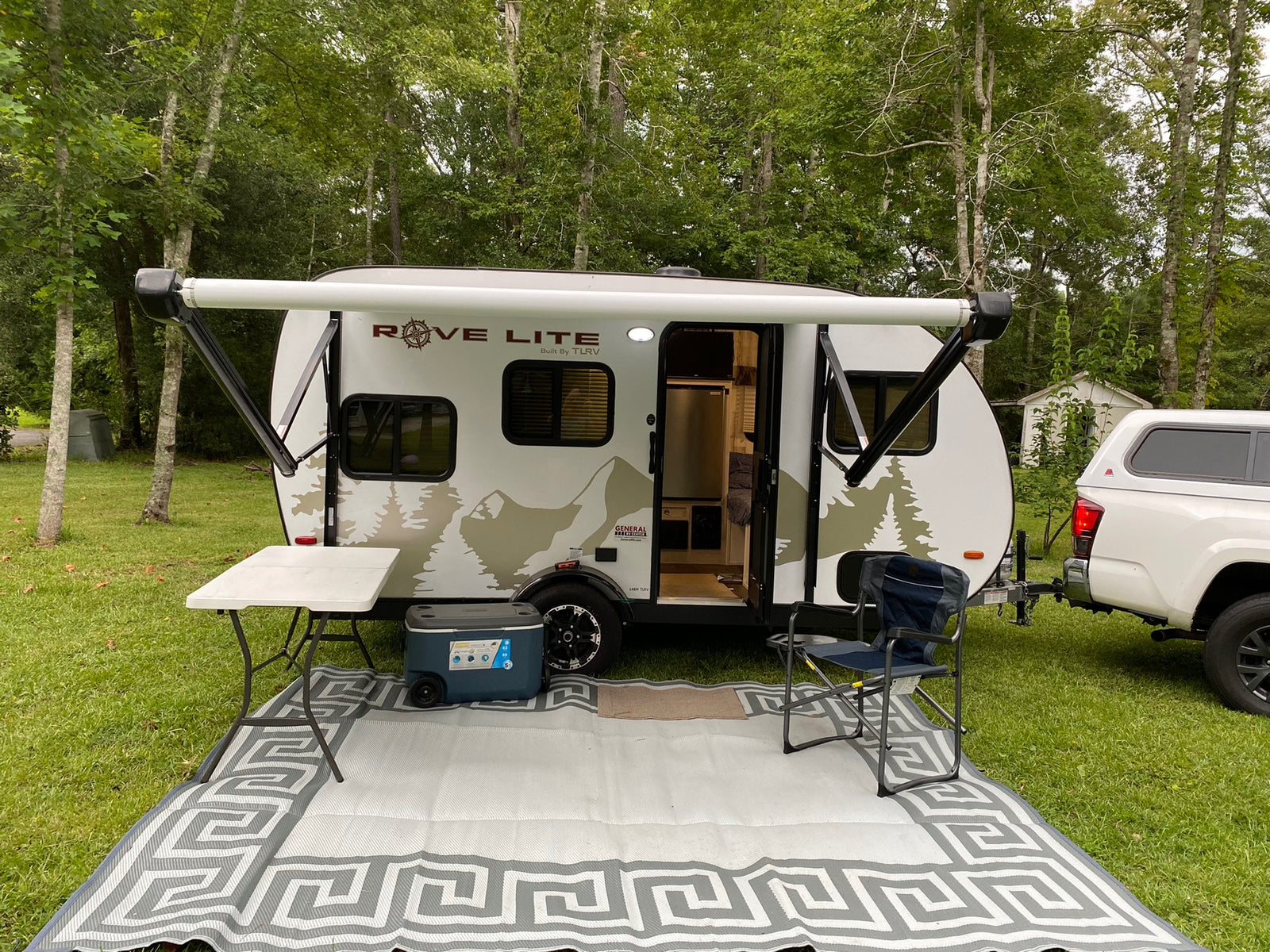 This RV rental travel trailer is ready for camping, set up with an extended awning, outdoor mat, table, and chair.