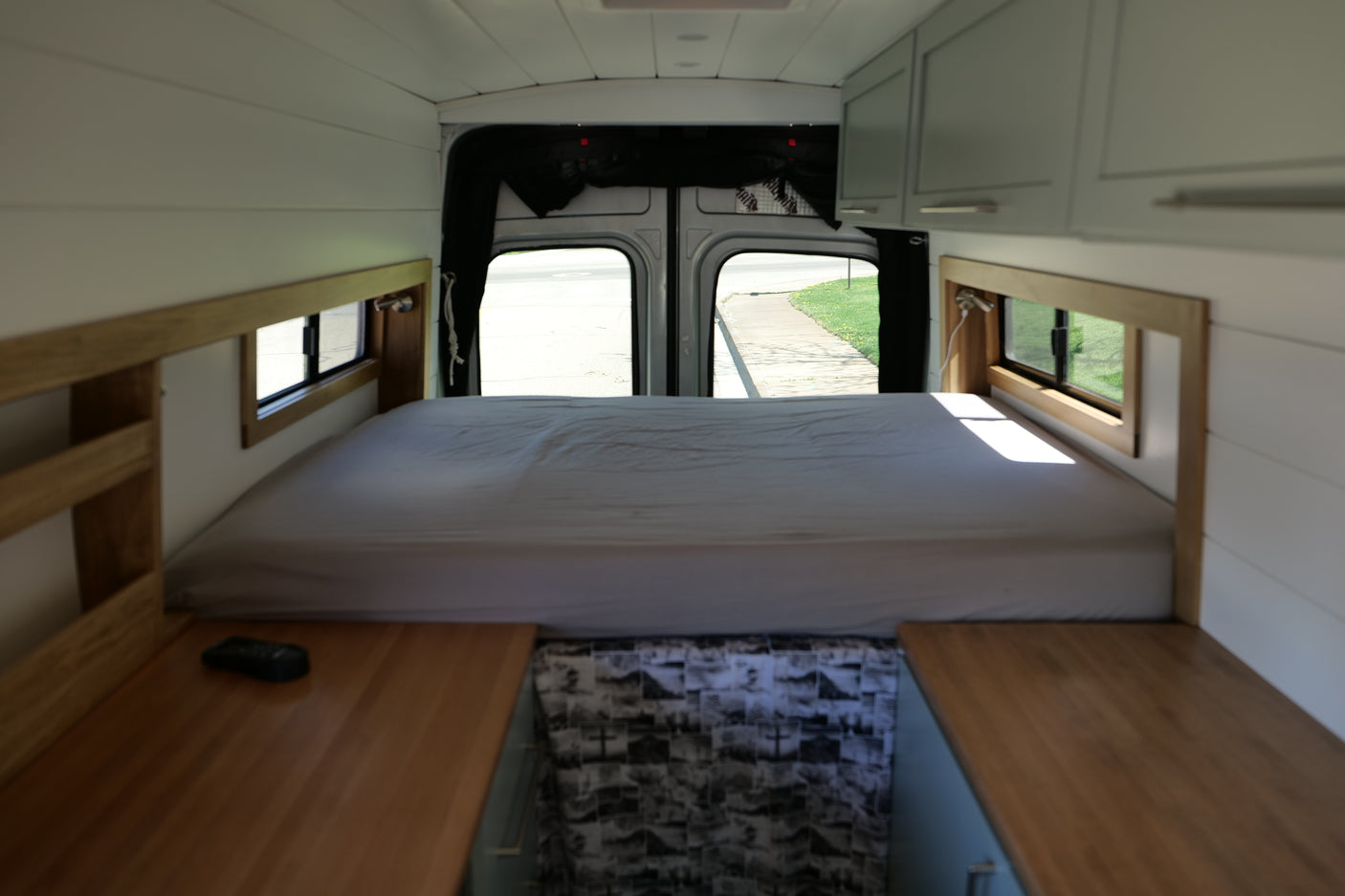 RV rental: Cozy camper van interior with a comfortable bed, wooden accents, storage, and natural light from rear windows.