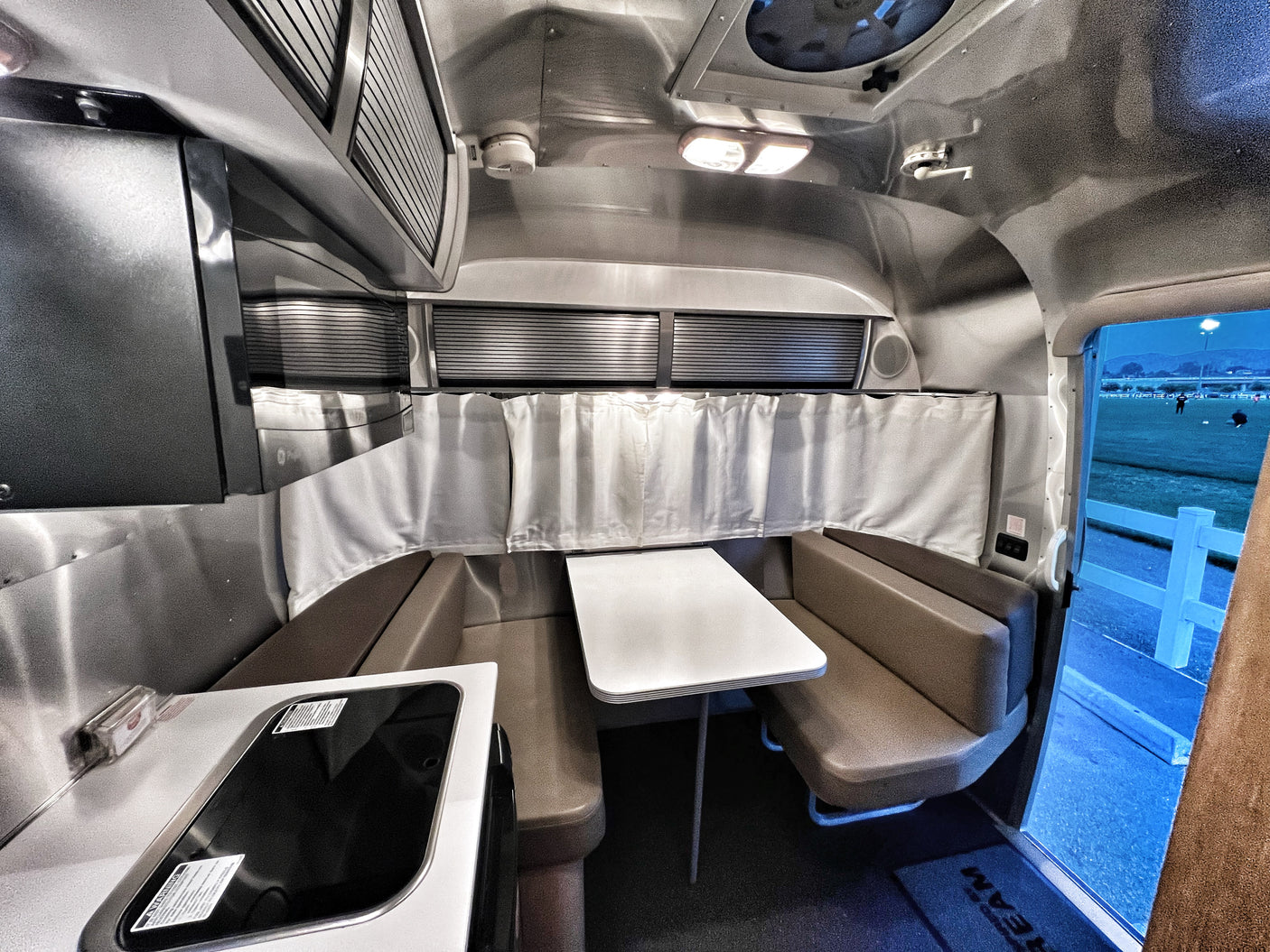 Inside a sleek Airstream RV rental, with dinette, kitchenette, and a view to an outdoor field. Ready for travel!