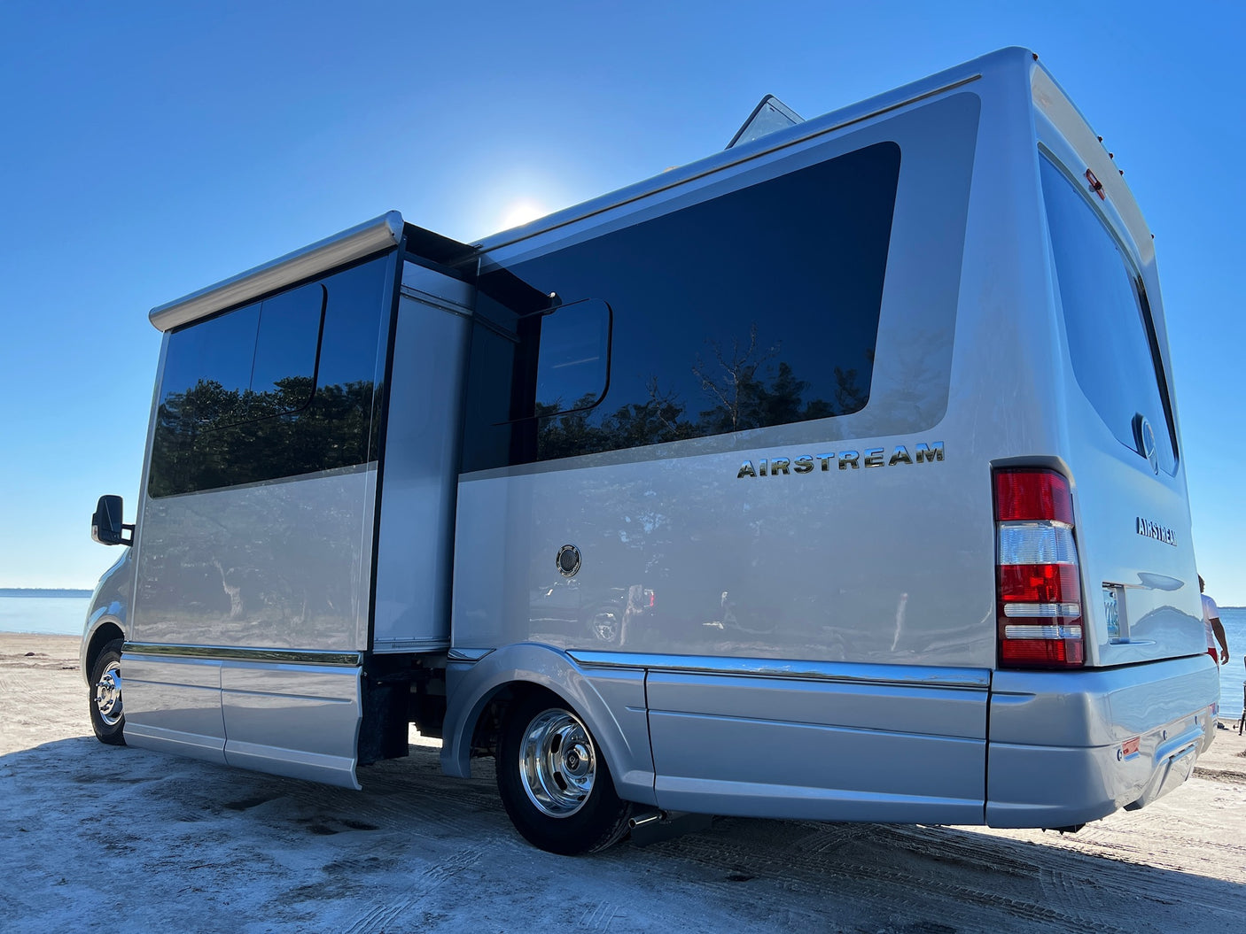 Silver Airstream RV rental parked on a sunny sandy shore, side open. Perfect for outdoor adventures and scenic travel.