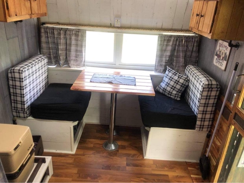 Cozy RV rental dinette with plaid benches, wood table, and window views. Perfect camper interior.
