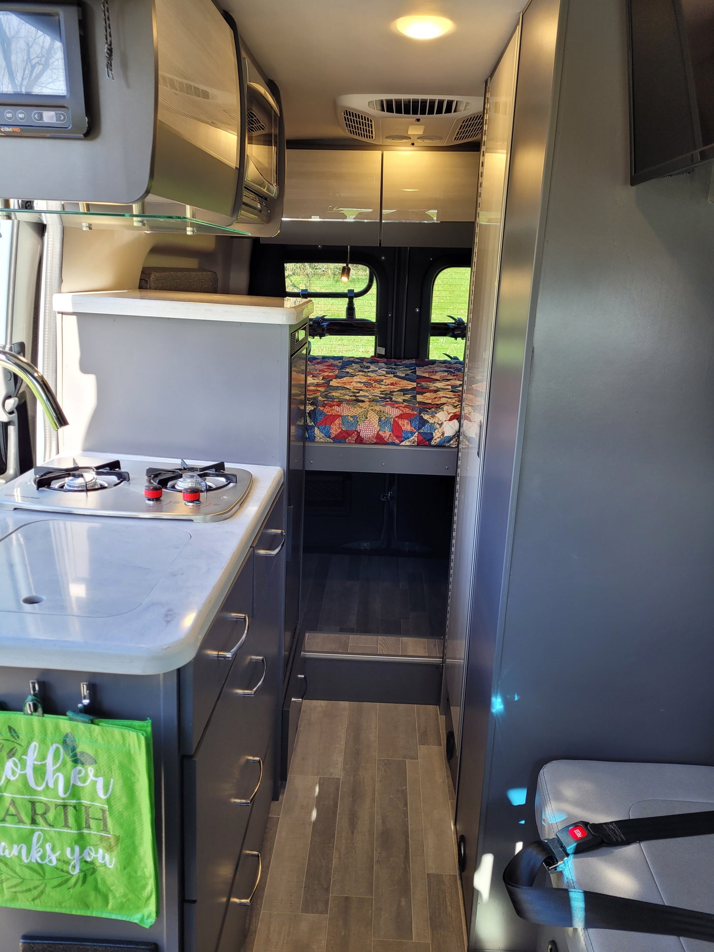 Visually, this RV rental's interior features a compact kitchen, a cozy bed with quilt, and bright overhead storage.