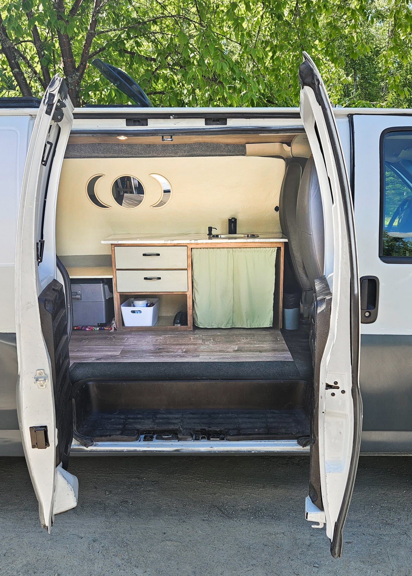 Inside a custom RV rental: compact kitchen with sink, unique moon decor, and wood-look flooring for cozy travel.