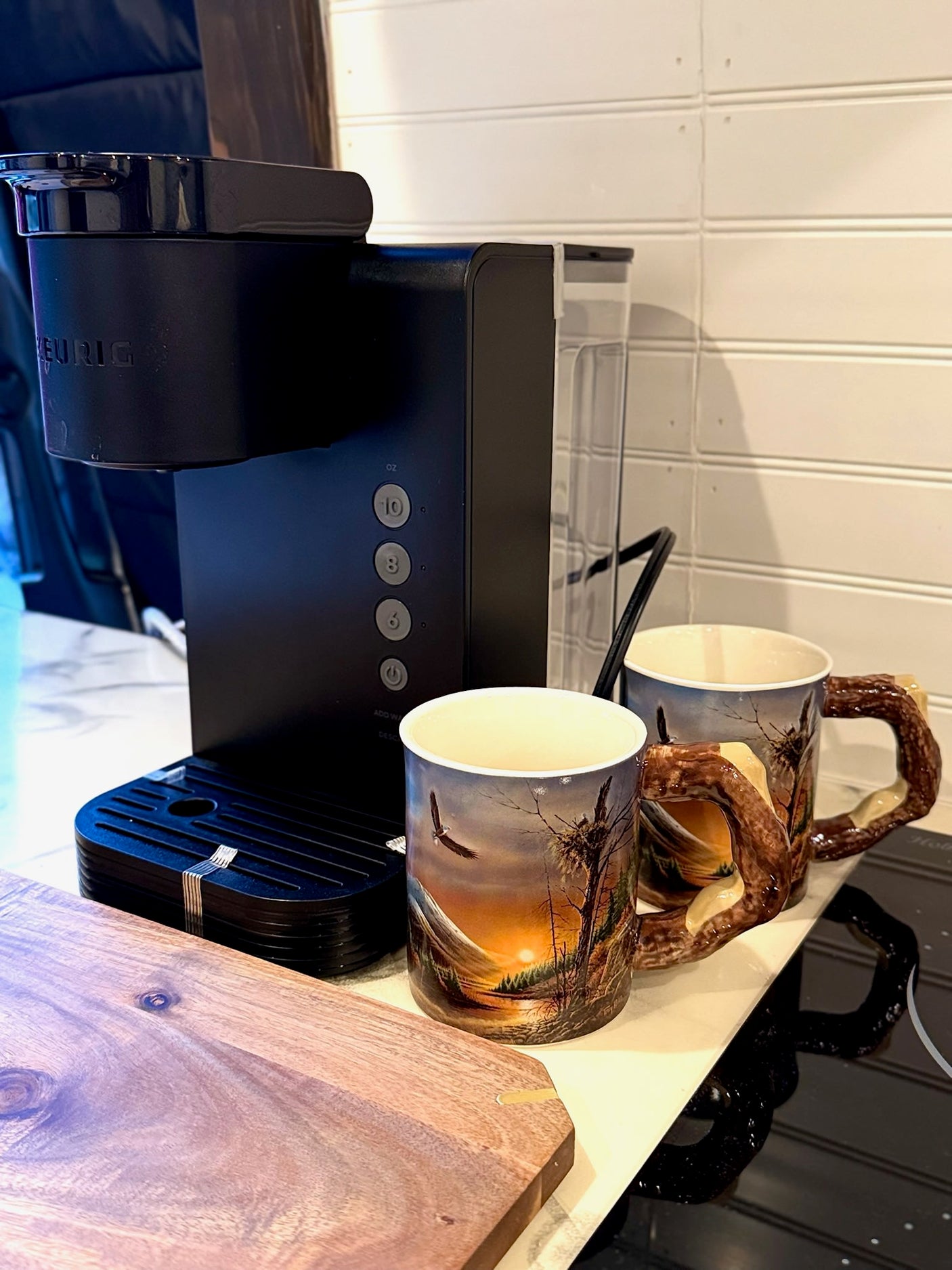RV rental comfort: Black Keurig coffee maker, nature-themed mugs, and a wooden board for your brew setup.
