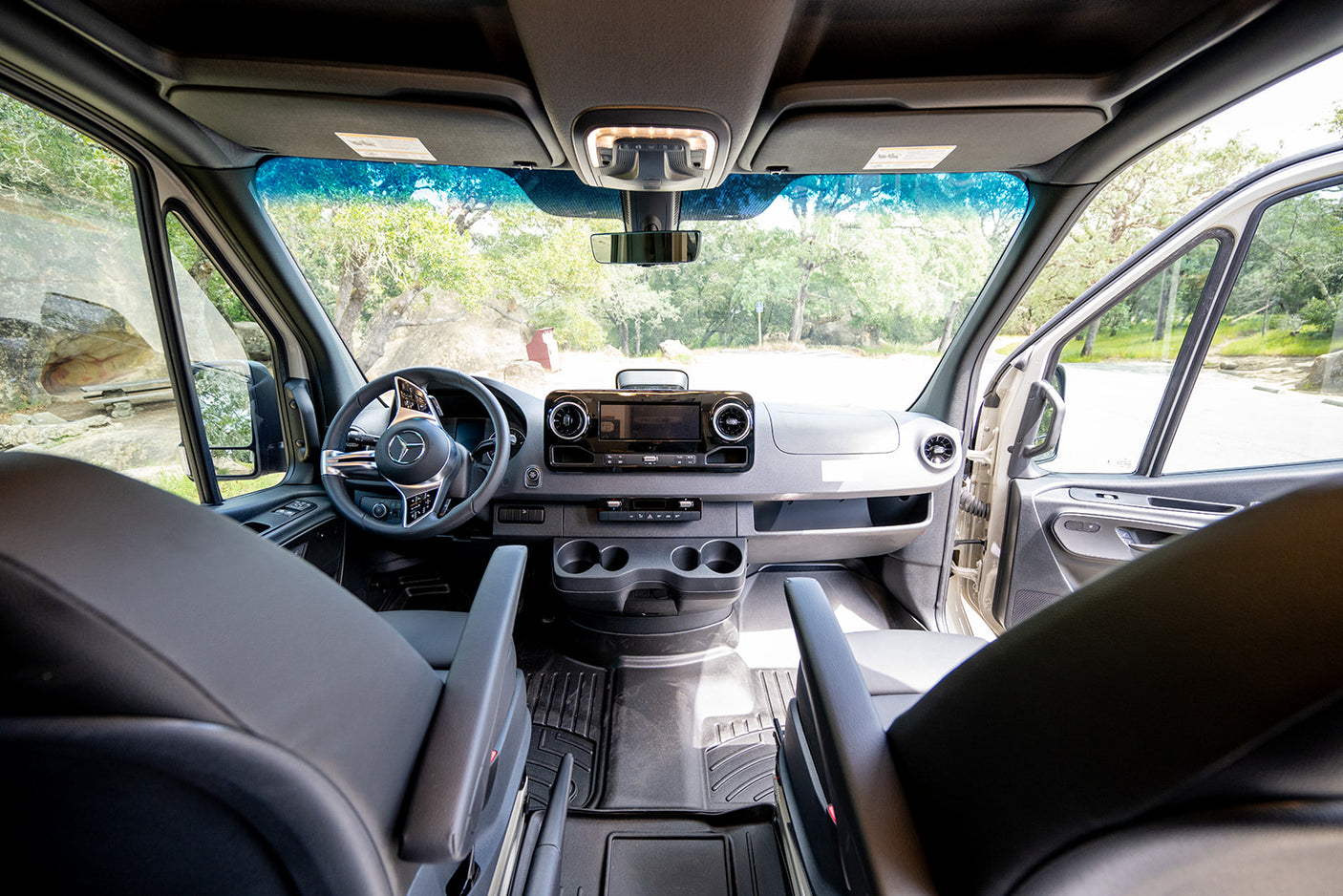 Modern Mercedes-Benz RV rental van interior: dashboard, steering wheel, front seats, and a clear view of nature outside.