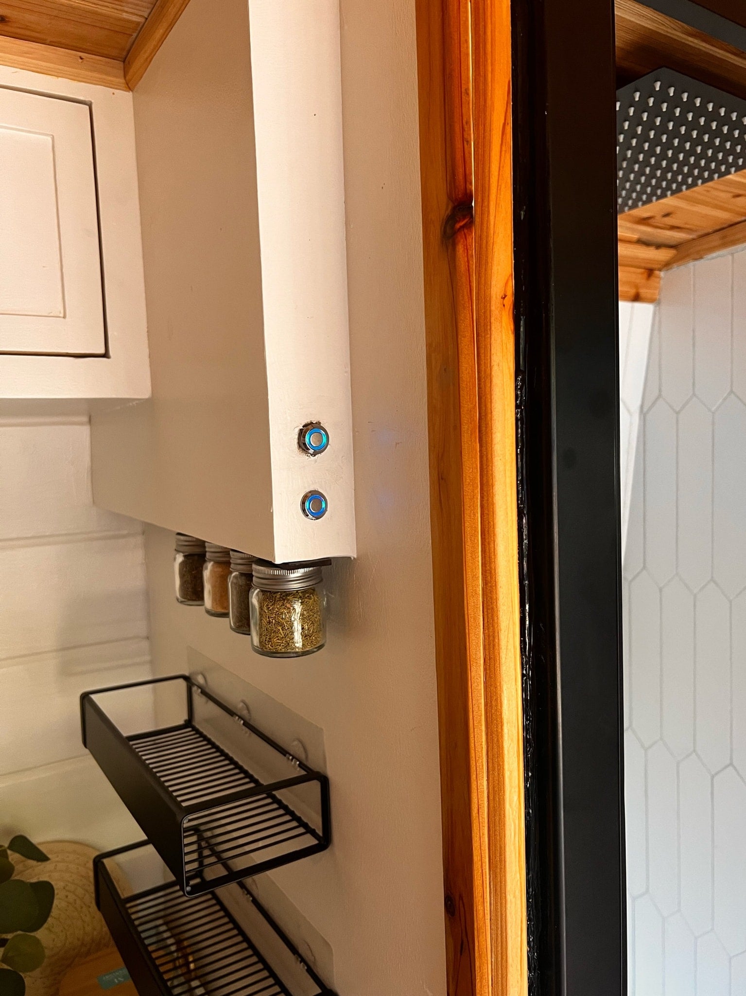 Compact RV rental kitchen with magnetic spice jars, smart storage shelves, and a glimpse of the shower. Efficient design.