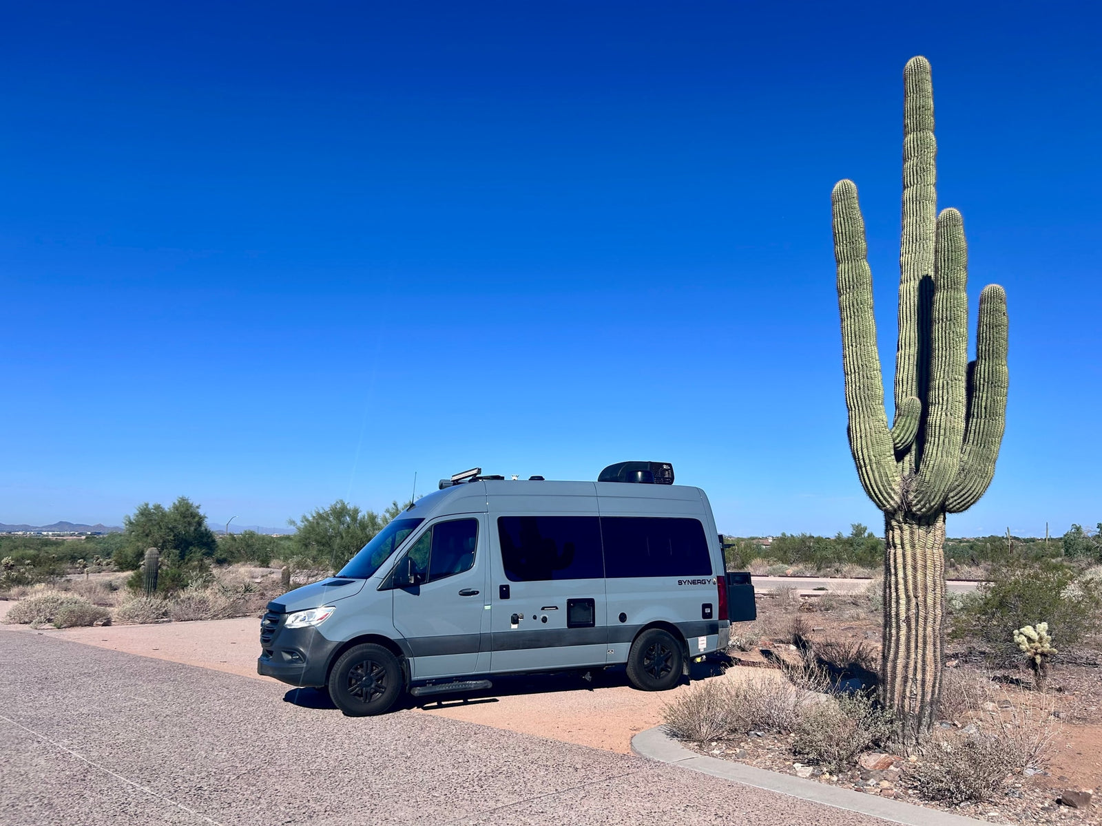 Gray RV rental next to a Saguaro cactus in a bright desert landscape with a clear blue sky