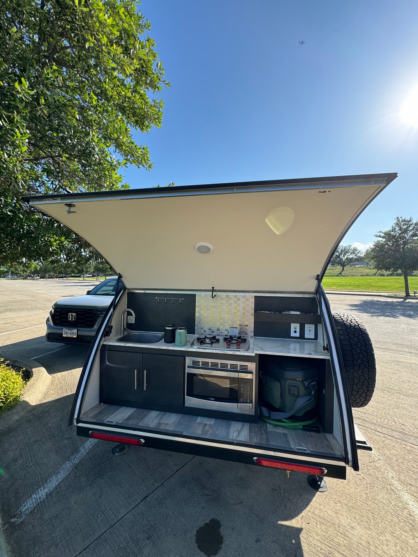 Teardrop trailer outdoor kitchen with sink, stove, microwave, and cooler. Ideal for an rv rental camping adventure.