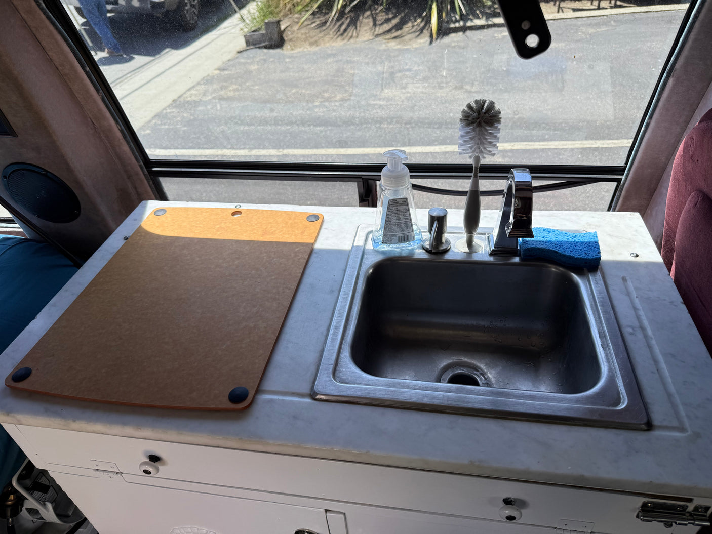 RV rental kitchen counter with sink, cutting board, soap, and brush, offering a convenient setup for guests.