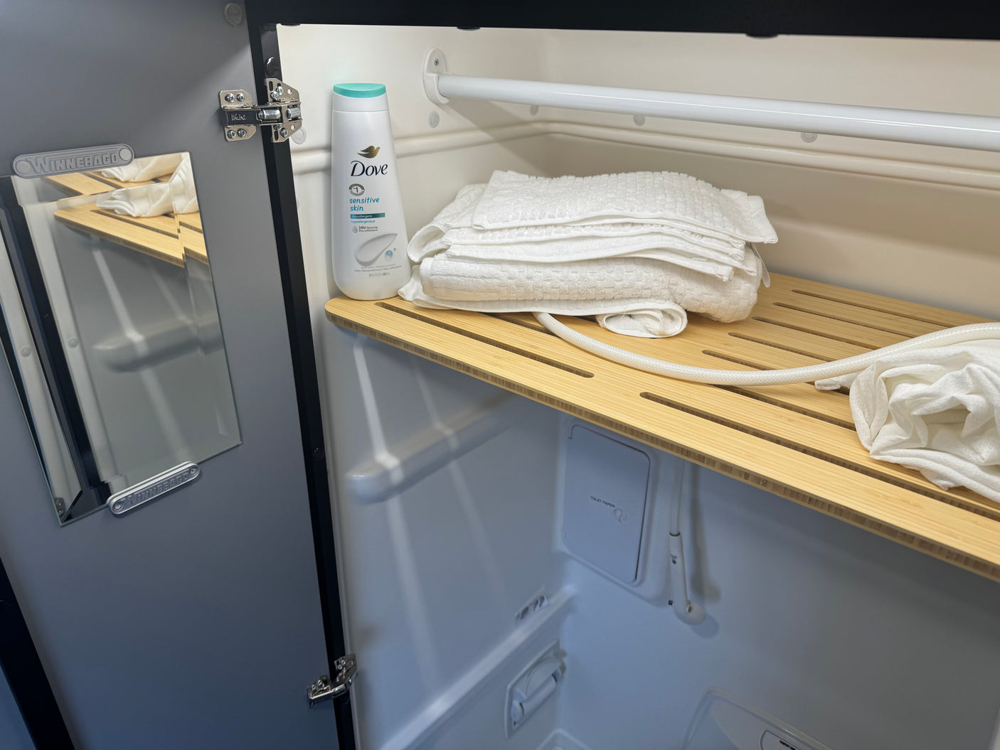 Winnebago RV rental shower with Dove body wash, white towels on a bamboo shelf, and a hidden toilet paper dispenser.