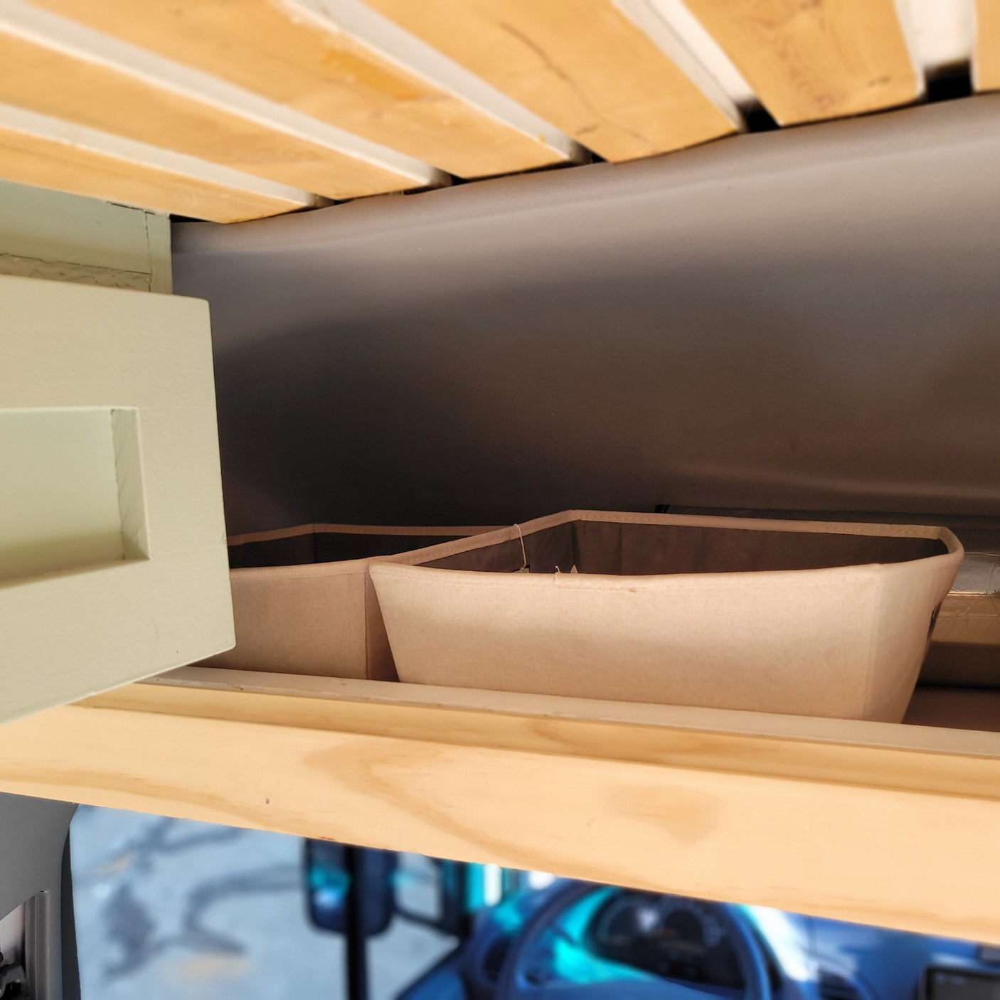 RV rental interior shows wooden bed slats, an open cabinet, and fabric storage bins, optimizing space inside.
