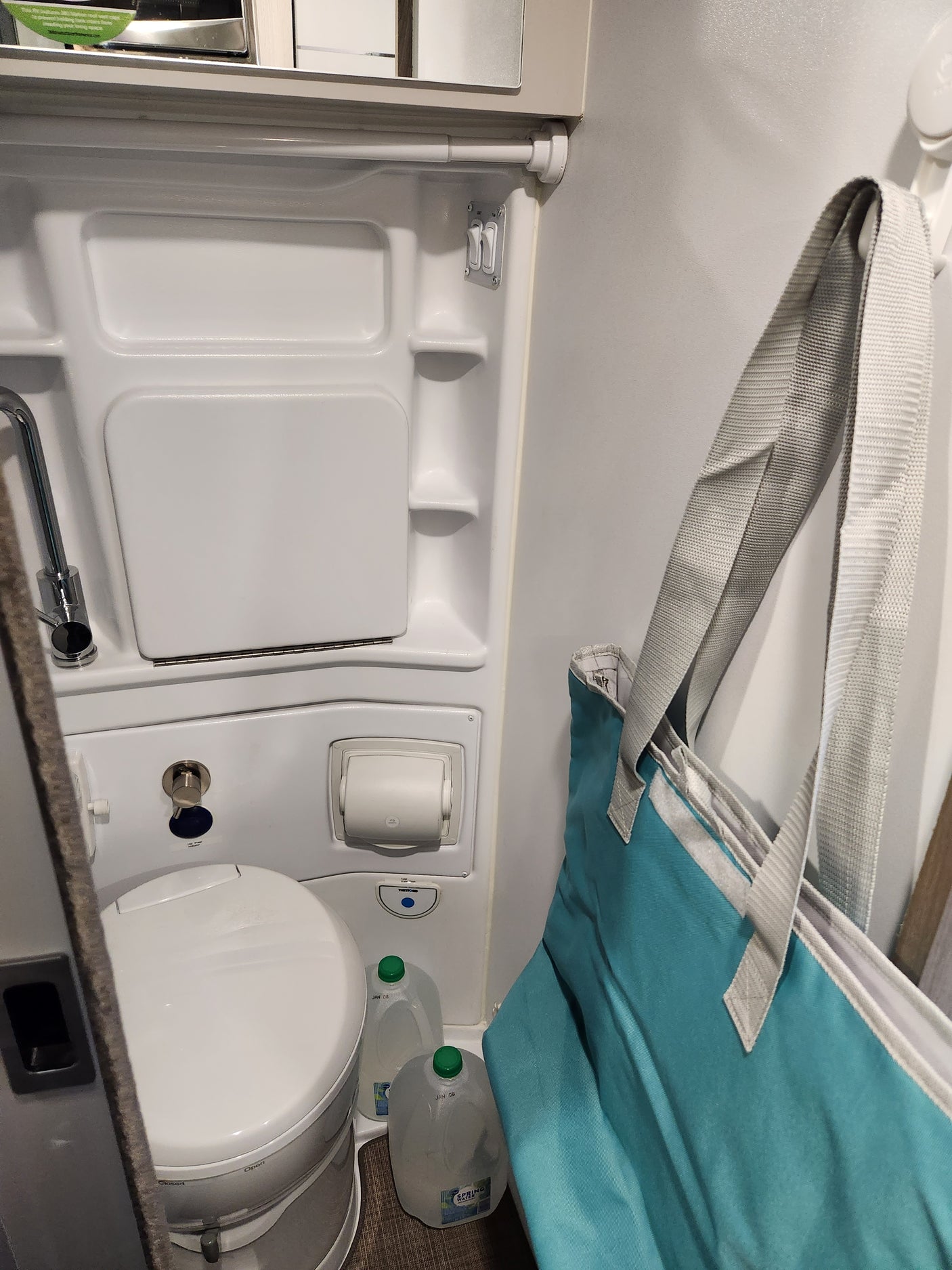 Compact RV rental bathroom: features a shower, Thetford portable toilet, and overhead storage. Ideal for travel.