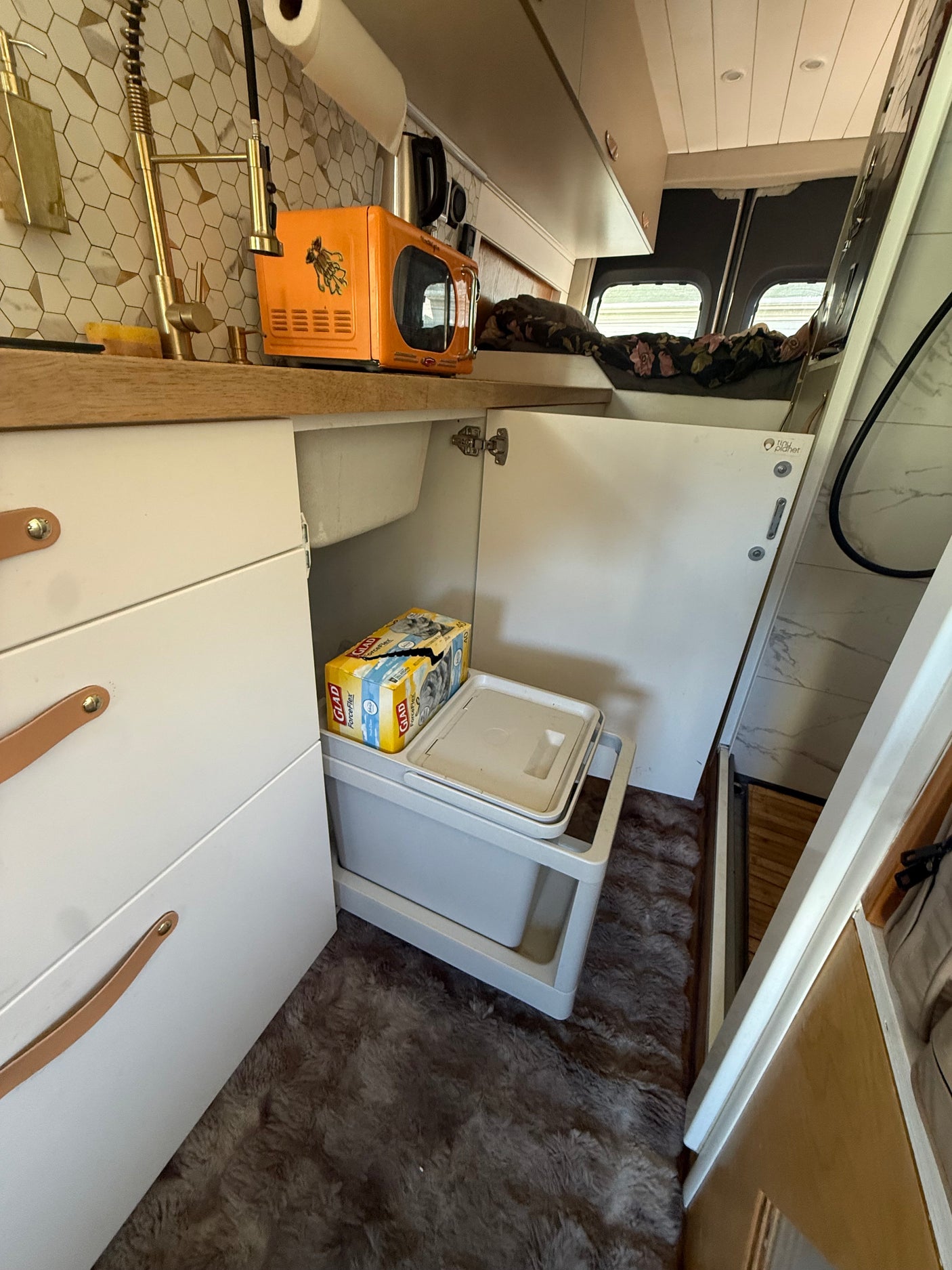 Functional RV rental kitchen with sink, orange toaster, and hidden pull-out storage for efficient van living.