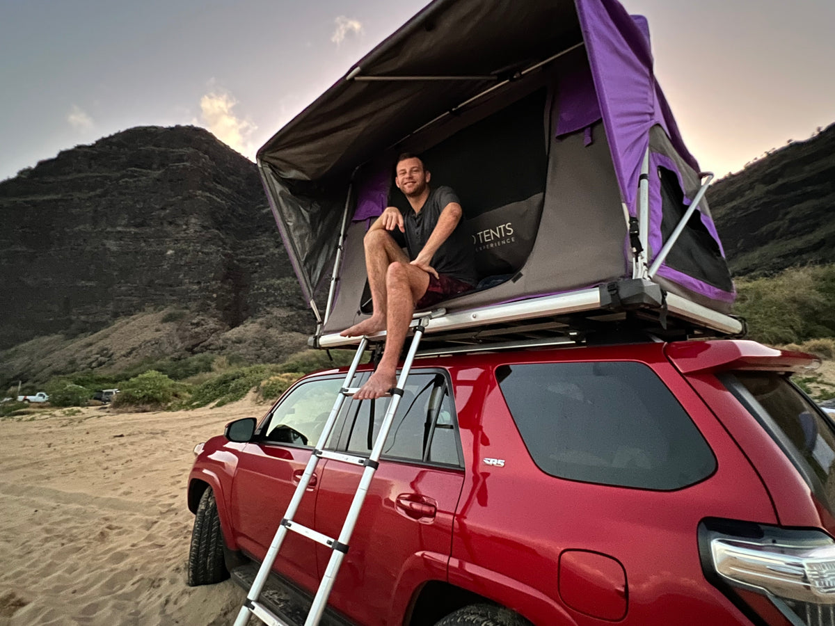Man smiles from his rooftop tent atop a red SUV. This RV rental offers camping by beach & mountains. — photo 8