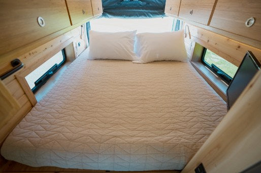 Cozy RV rental interior featuring a comfortable bed, overhead cabinets, and side windows, ideal for travel.