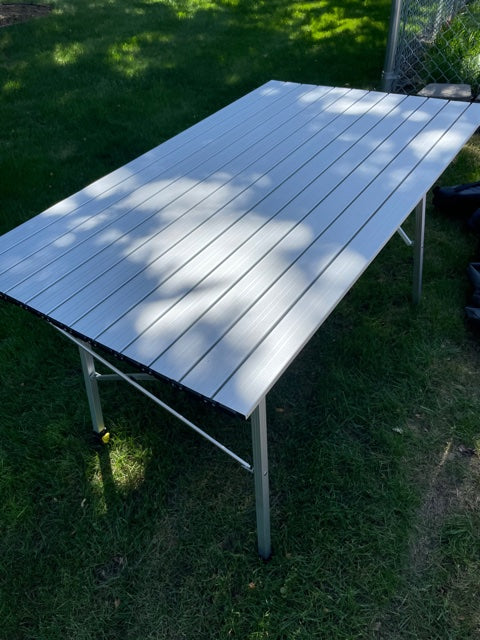 Portable aluminum camping table set on green grass, ideal for your RV rental trips. Features a slatted surface.