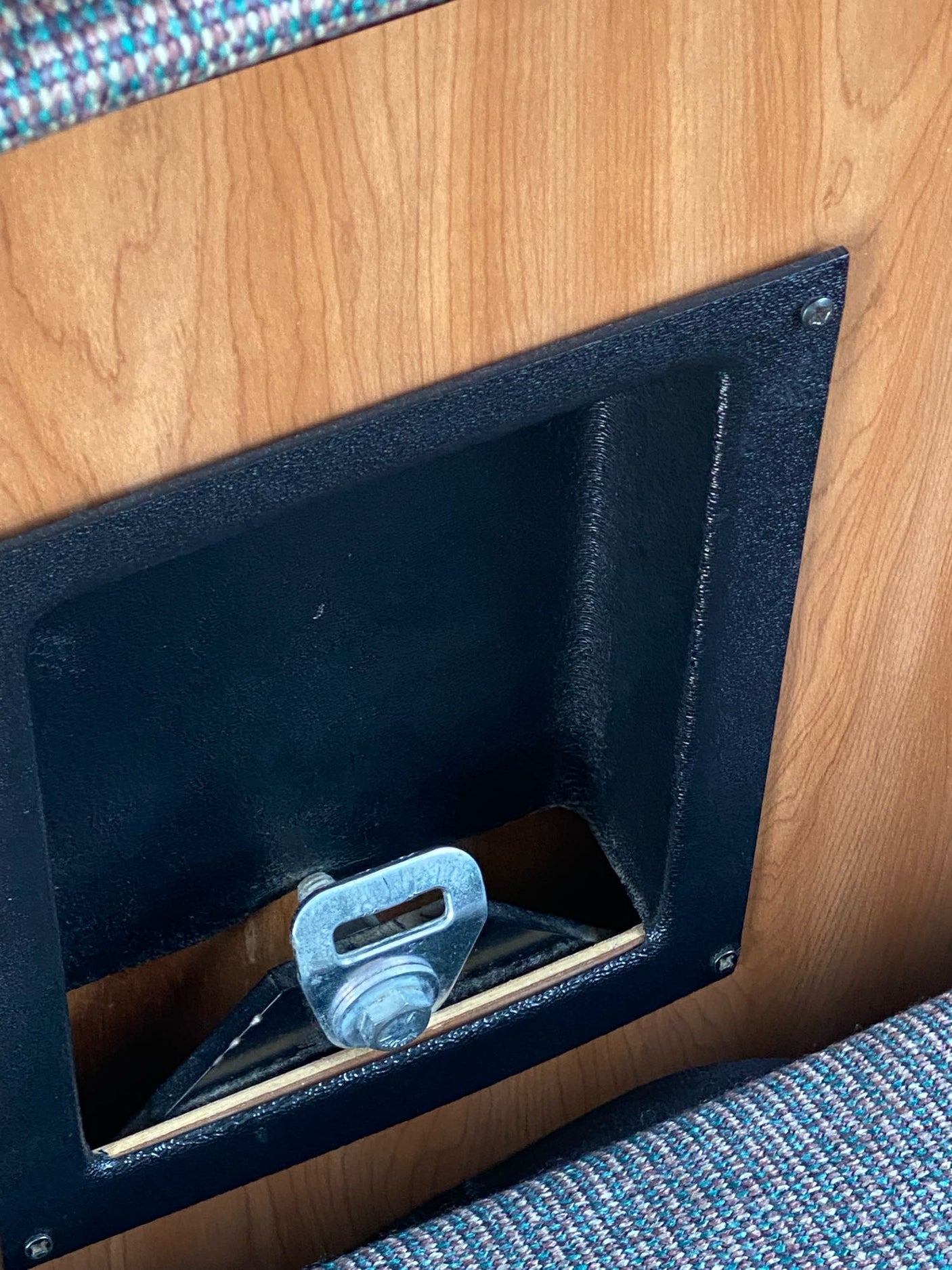 RV rental safety: A silver seatbelt mechanism mounted in a black recessed box on a wooden wall, with patterned fabric upholstery.