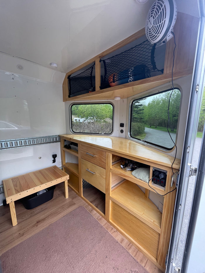 Inside a custom RV rental: light wood cabinetry, dual windows with scenic views, and smart storage for travel comfort.