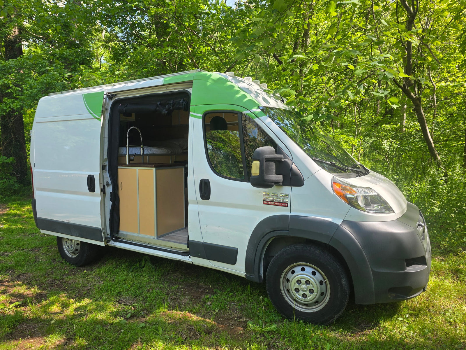 This white Ram ProMaster camper van with green accents & open side is ready for your next RV rental road trip in nature.