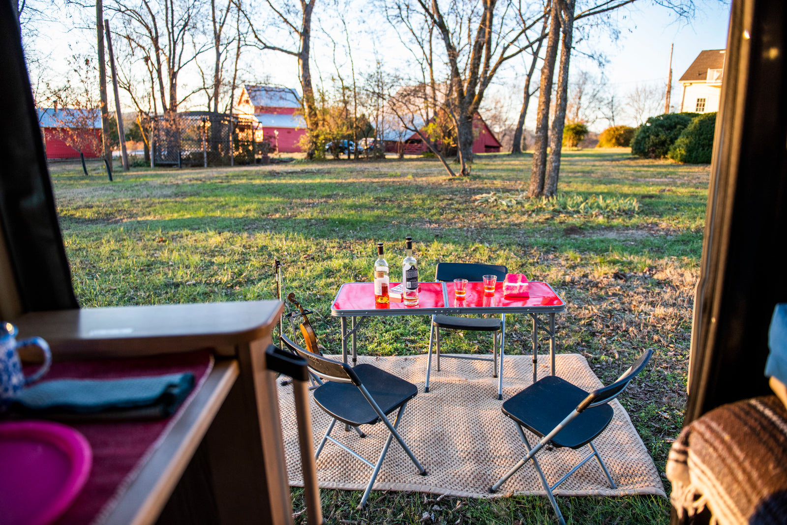 RV rental view: Relaxing outdoor setup with a table, chairs, drinks, and a violin at sunset in a grassy field.