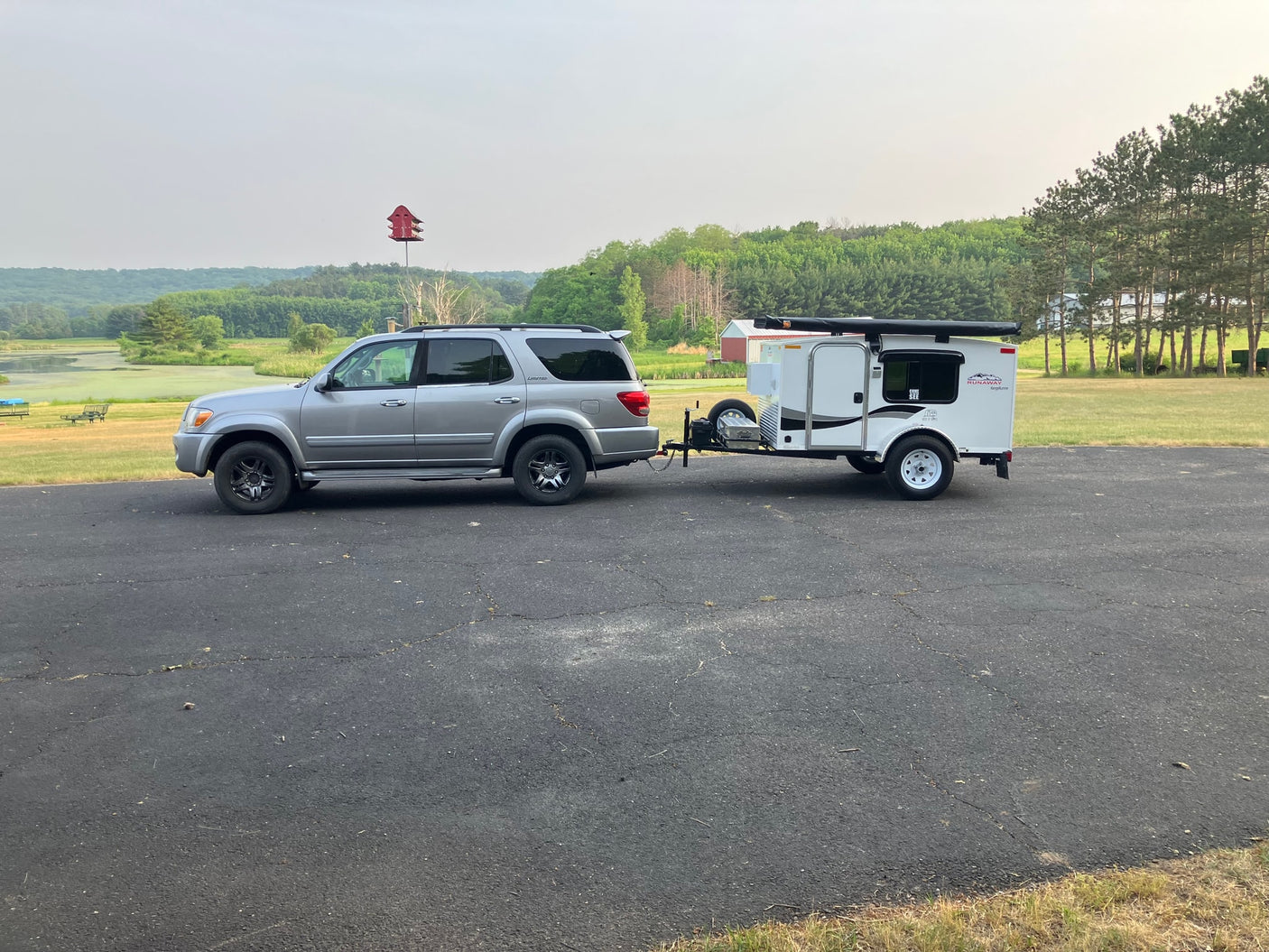 Silver SUV towing a Runaway RV rental travel trailer on a paved driveway, ready for outdoor adventures by a scenic pond.