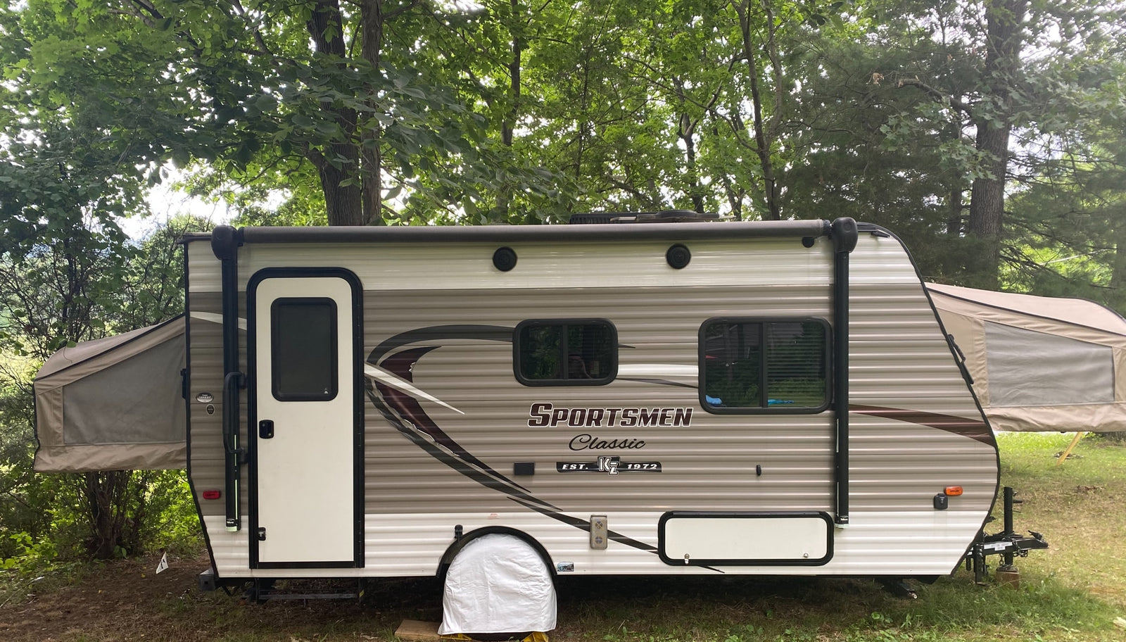 This Sportsmen Classic hybrid RV rental is set up for camping in a wooded area, with its tent-like bunks extended.