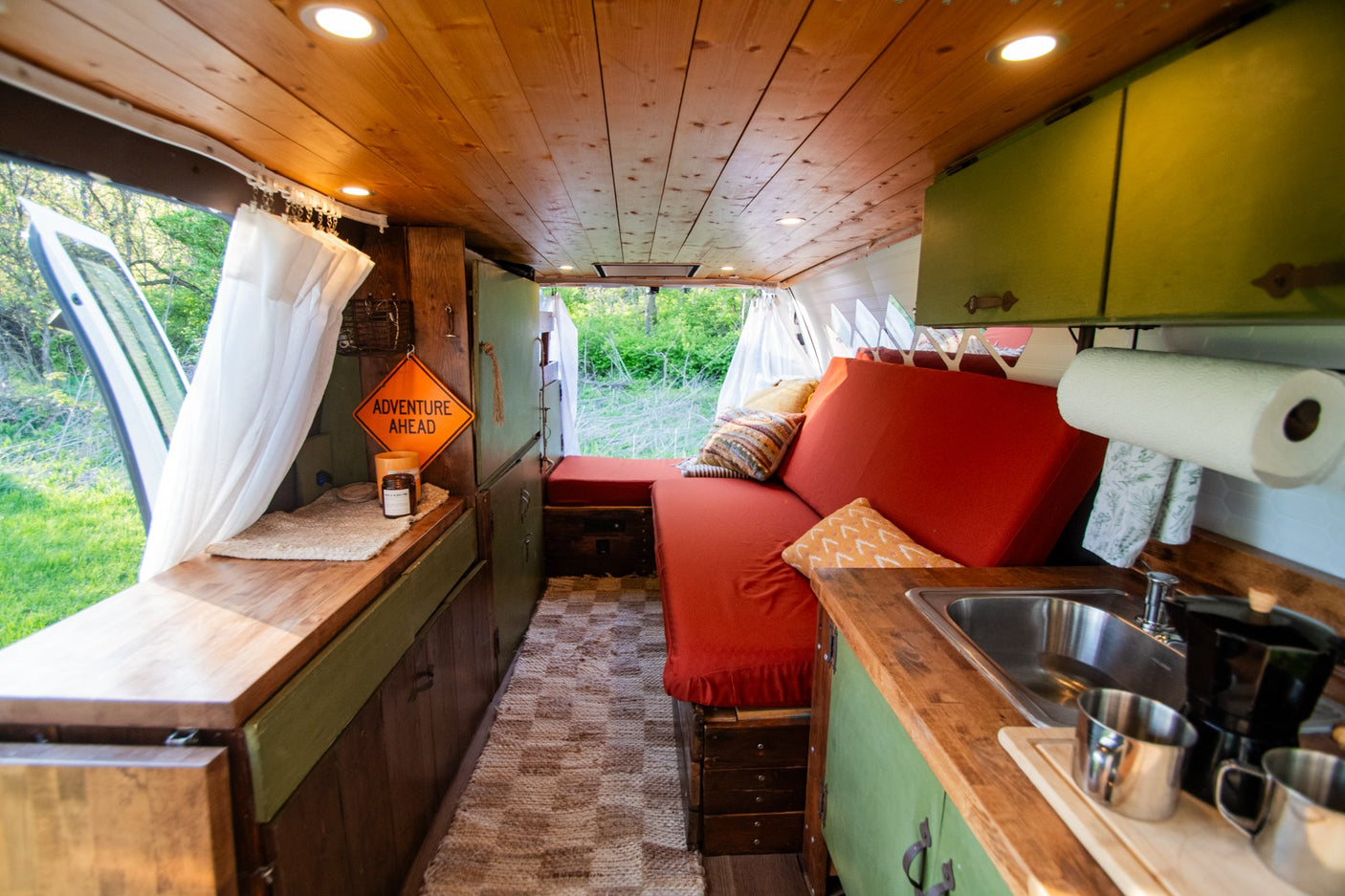 Step into this custom rv rental camper van. Warm wood and green interior, red seating, kitchen, and a view to the outdoor adventure.