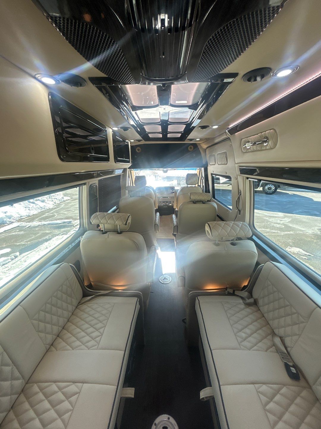 parked on a snowy lot under a clear sky. Ready for your next adventure!|Luxurious RV rental interior featuring a cream quilted captain's chair with black piping and a snowy view outside.|Step into luxury with this custom rv rental van. Spacious interior features cream quilted seating