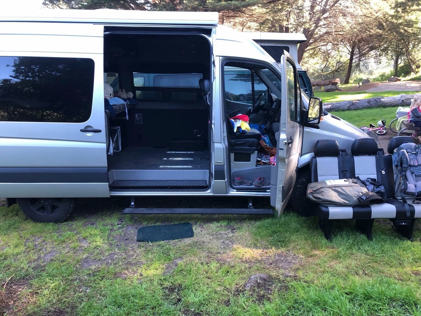 parked next to a vineyard with rolling hills and a clear sky.|Adventure-ready RV rental. Silver camper van with open doors