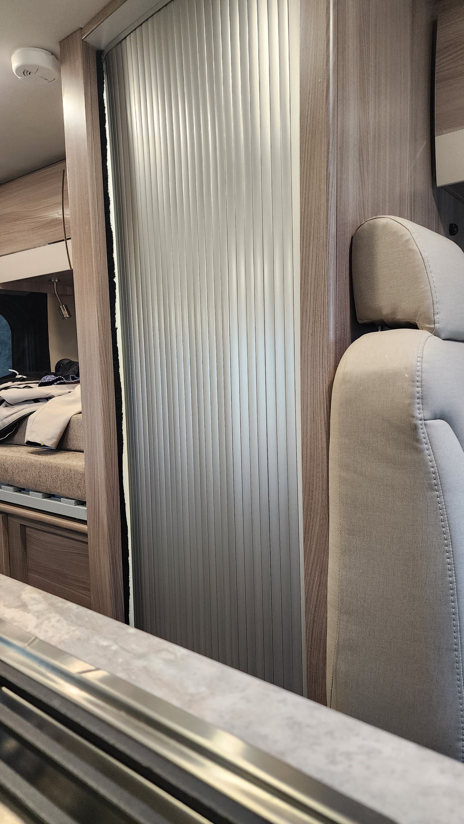 Upward view in an rv rental showing a comfortable bunk with beige upholstery, wood accents, and an aluminum roll-up window blind.
