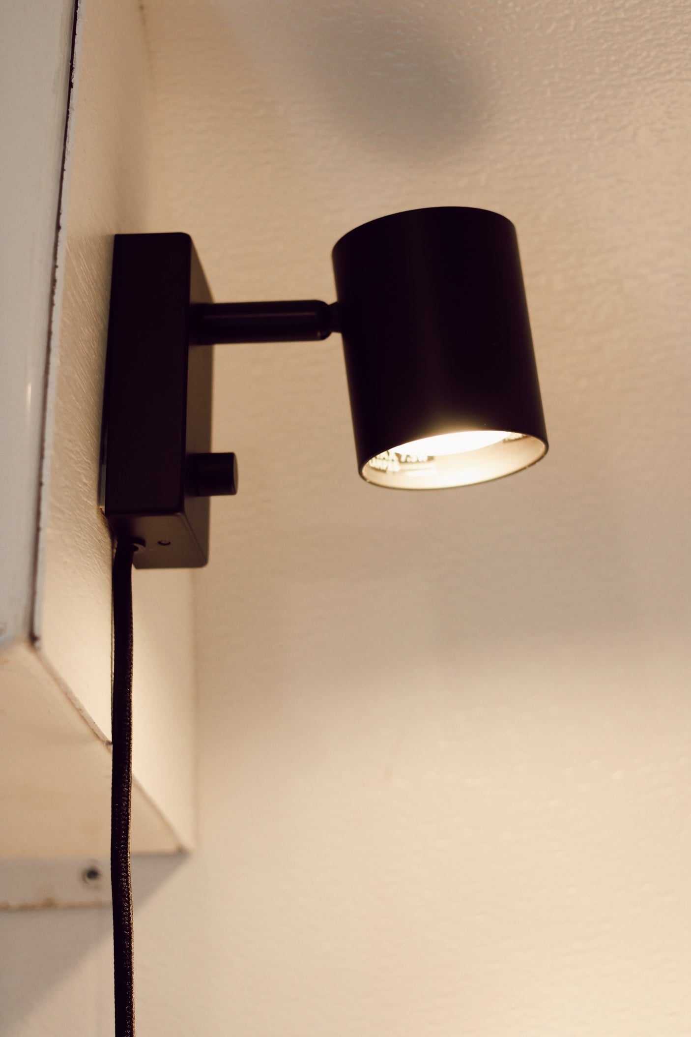 Compact black wall lamp providing warm light in an RV rental interior. Perfect for cozy reading nooks.