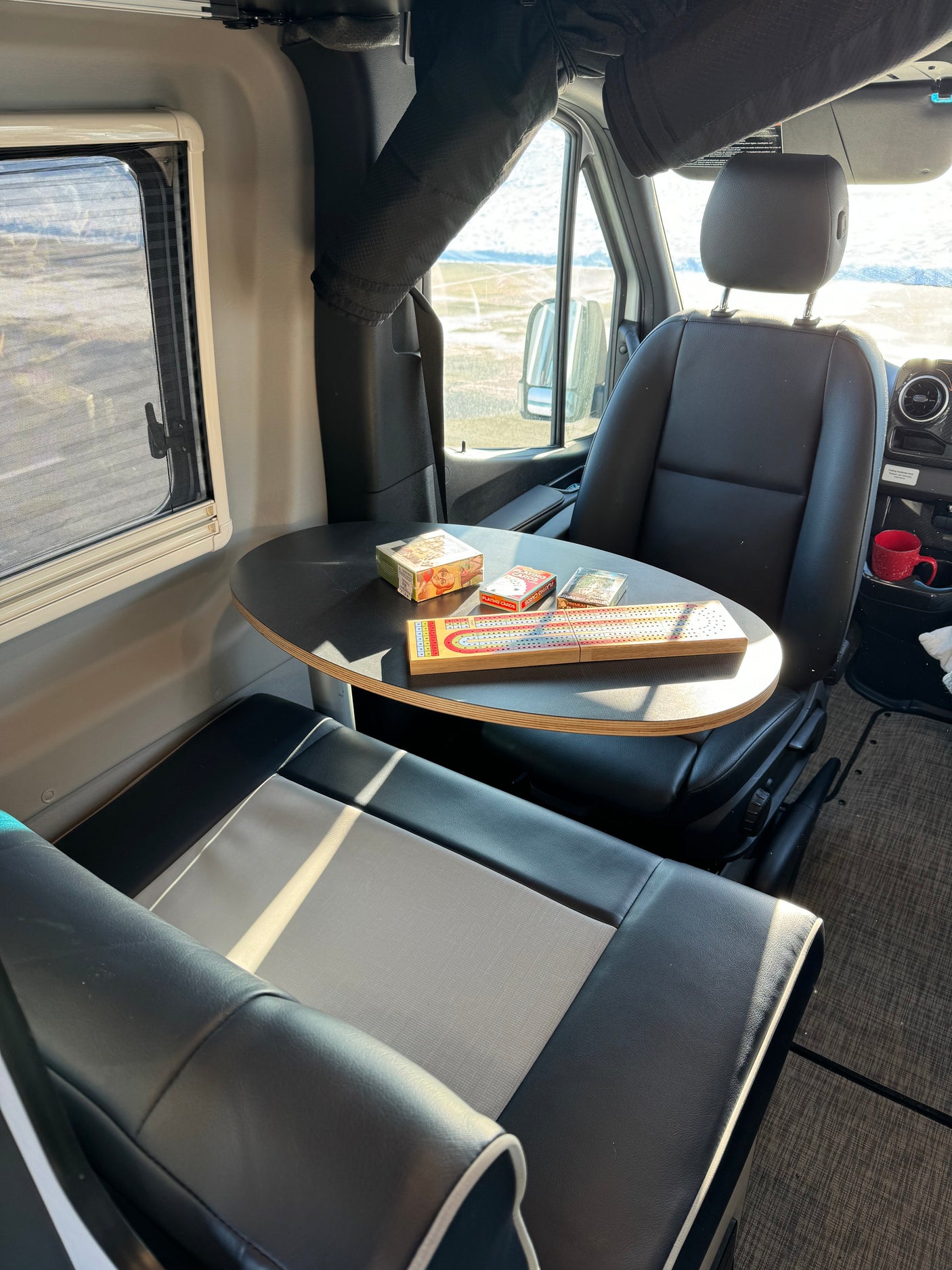 Relaxing in an RV rental: A cribbage board & cards are set on a table between two comfy seats, overlooking outside views.