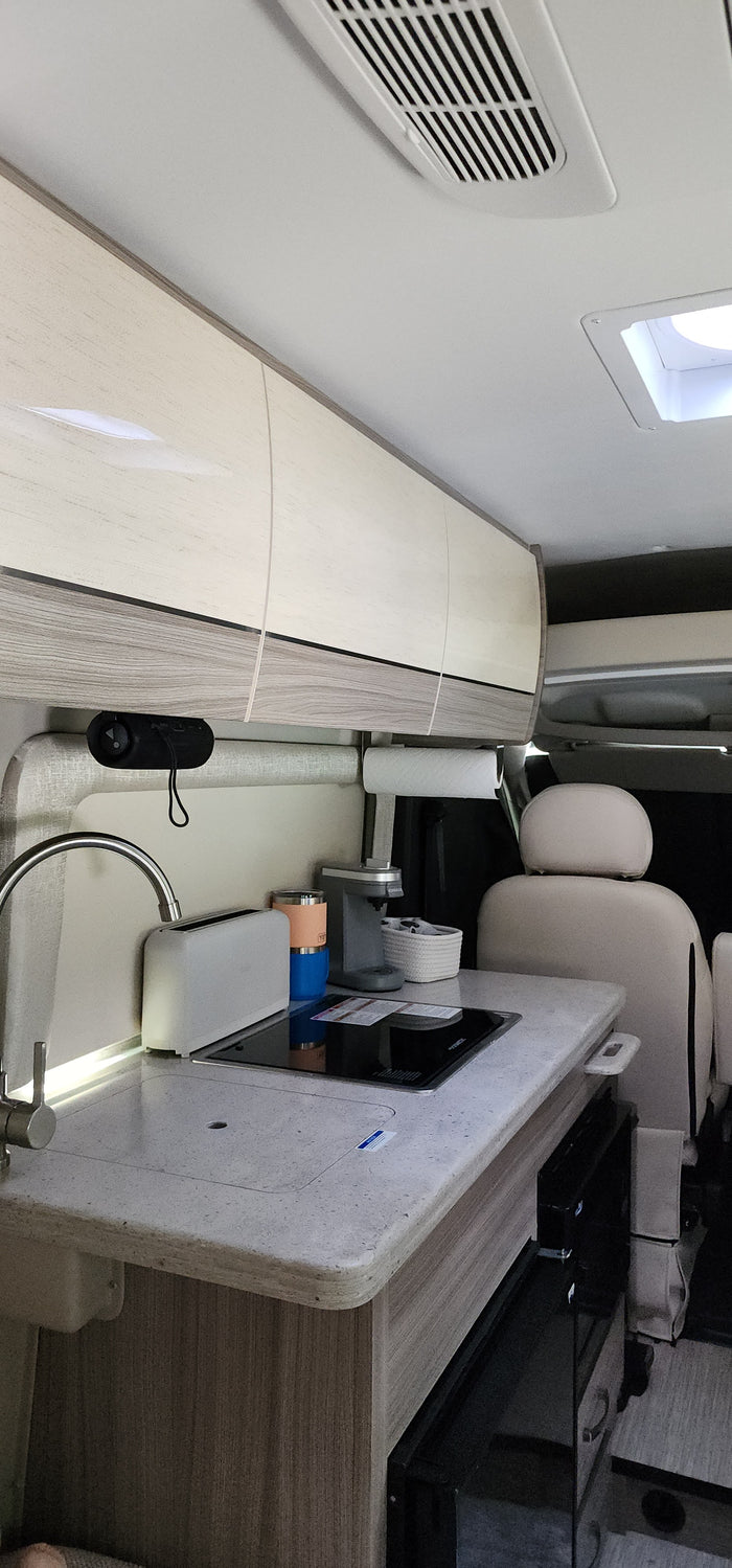 Inside this RV rental, find a compact kitchen: sink, induction cooktop, coffee maker, & overhead cabinets. Ready for adventure.