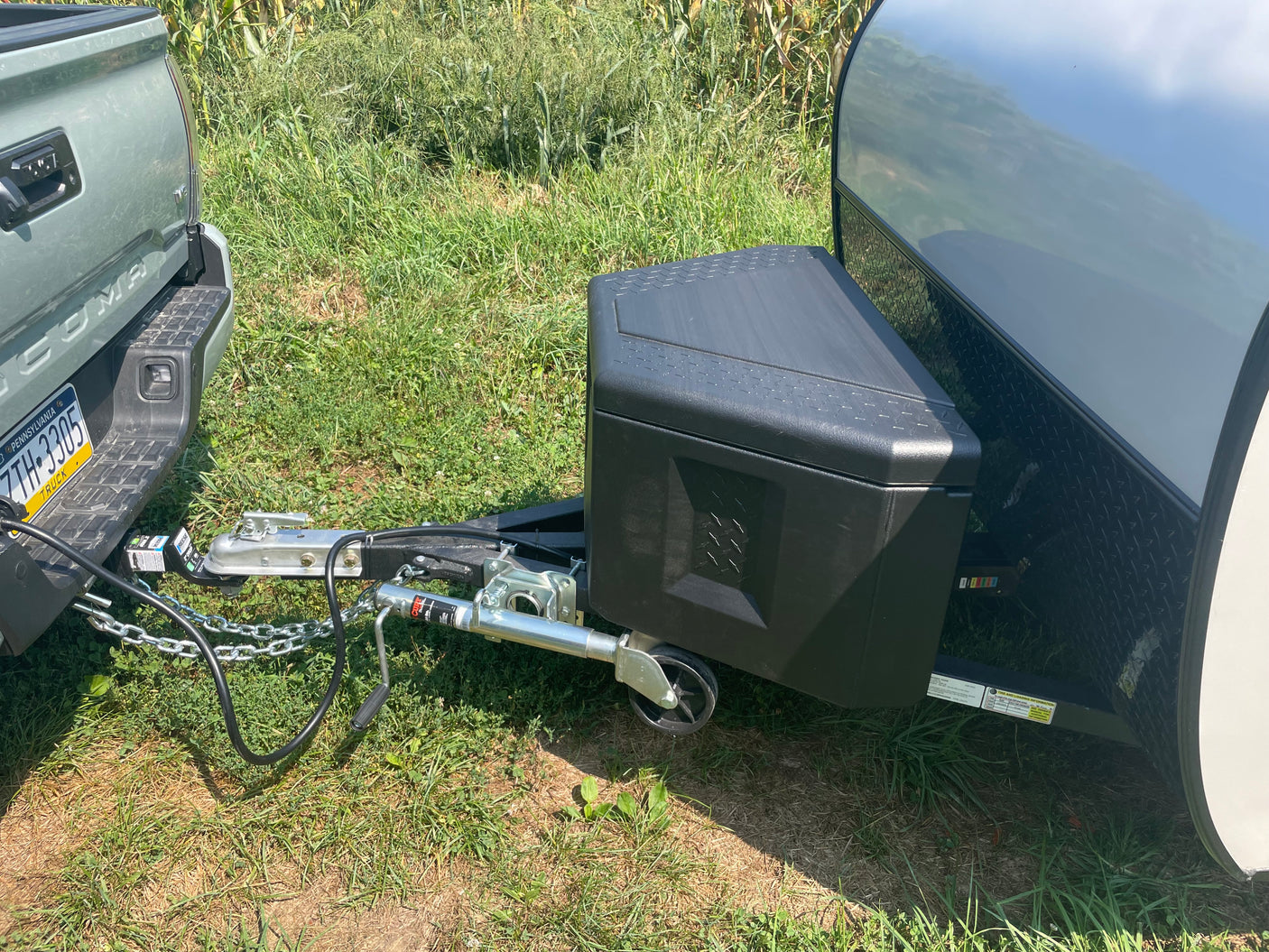 Green truck hitched to a small travel trailer, ready for an RV rental adventure in a grassy field.
